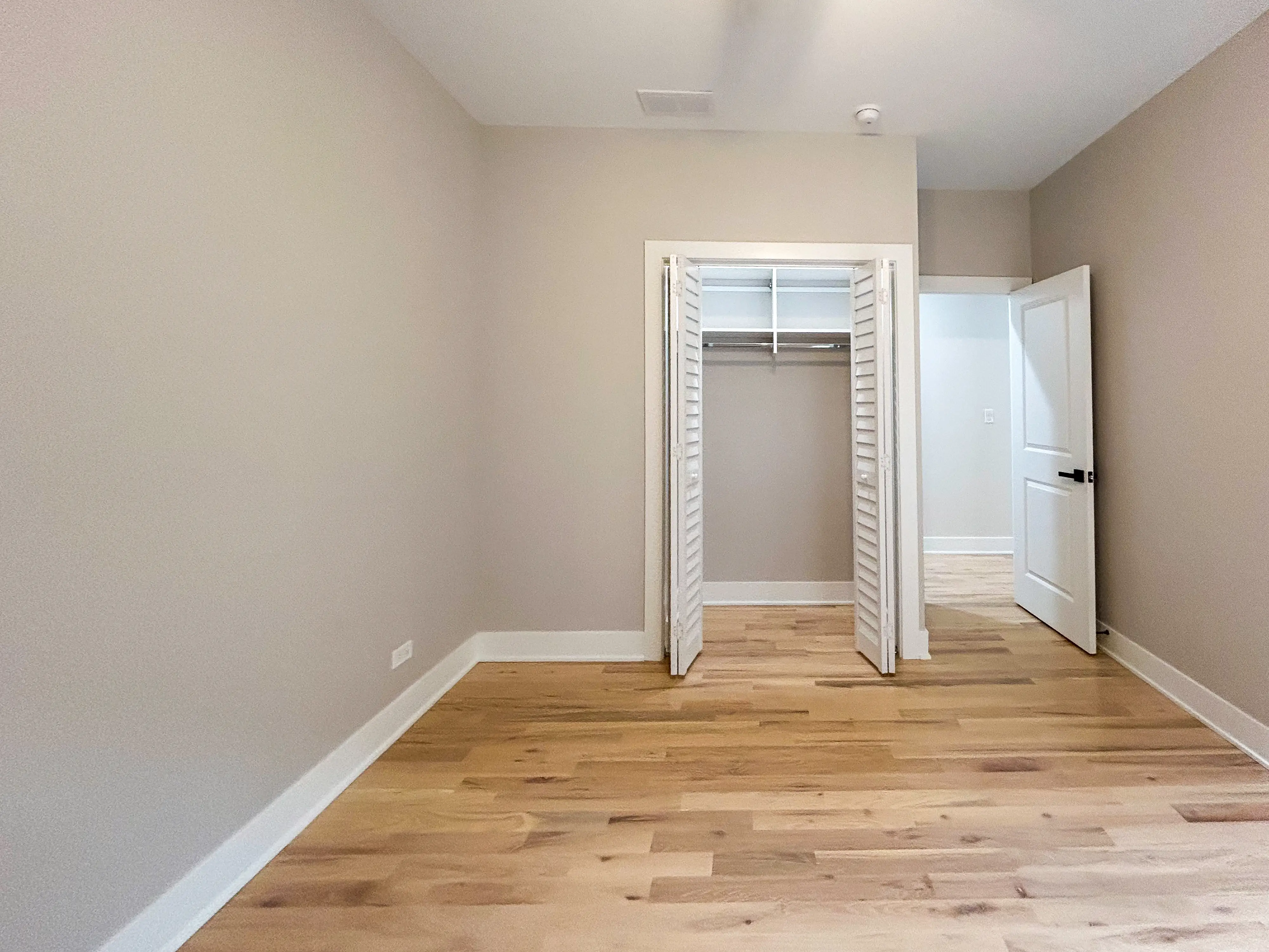 Inside an empty bedroom with wood floors, a closet, and an open door on the right