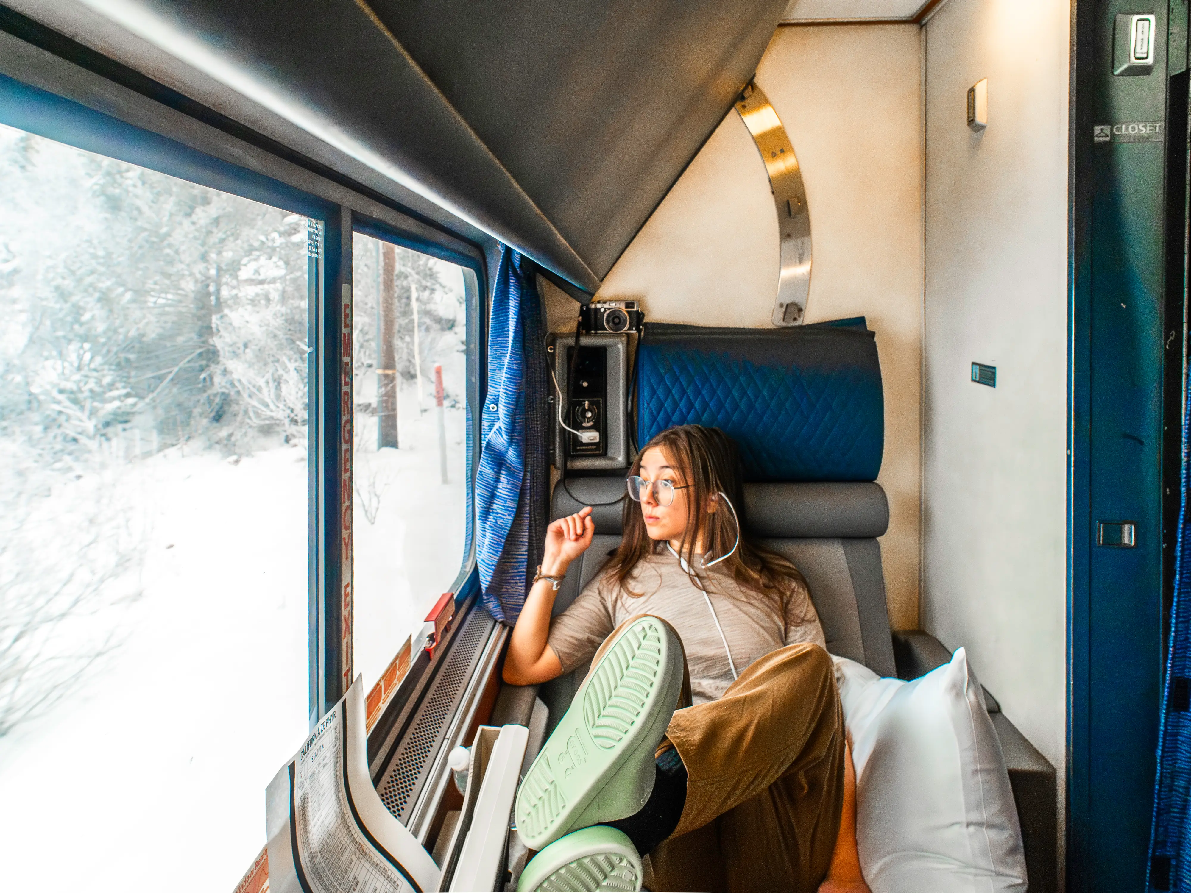 The author sits with her feet up in an Amtrak roomette looking out a window to the left