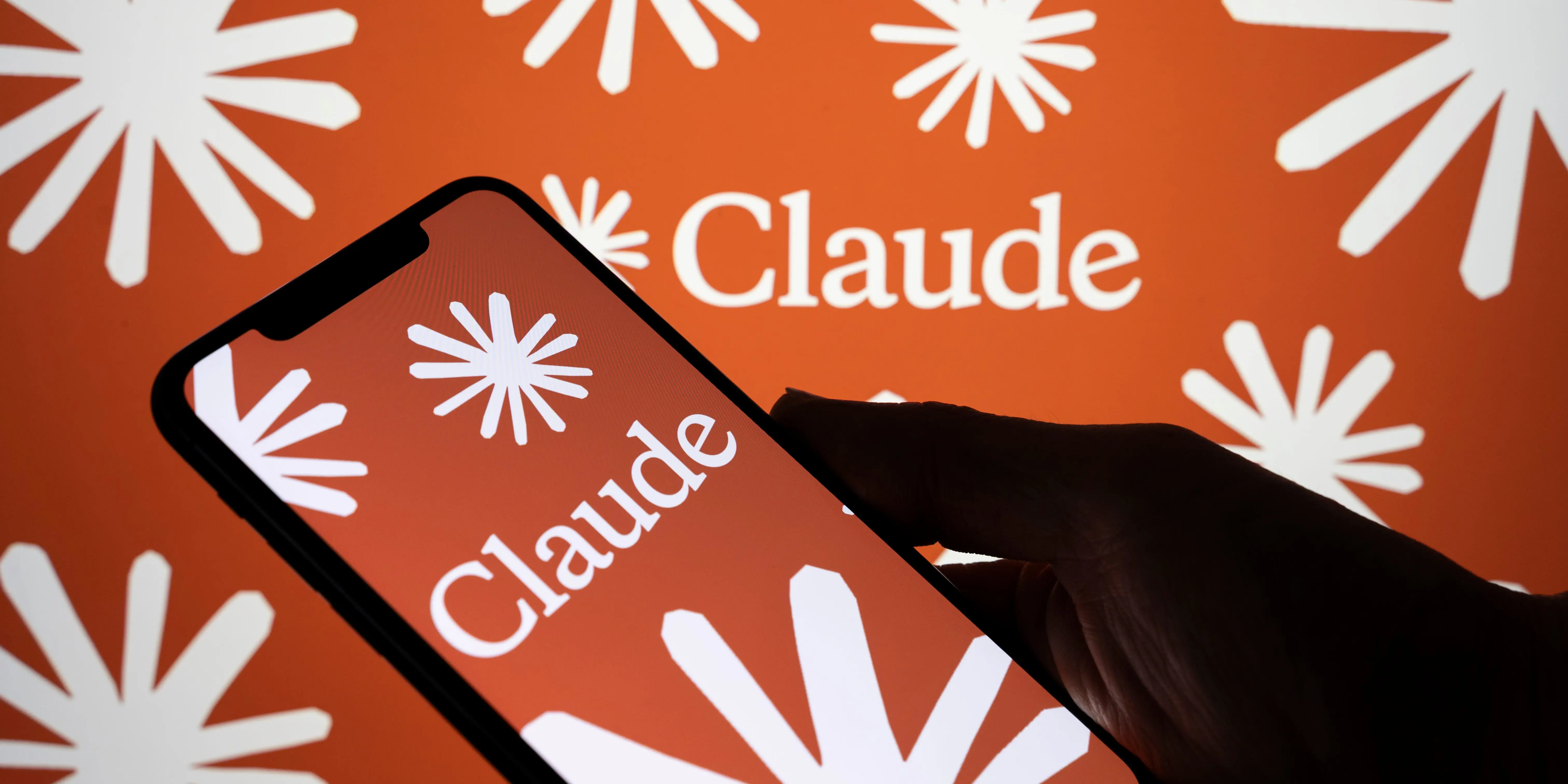 A dark figure holding a phone with Claude's emblem on the screen.