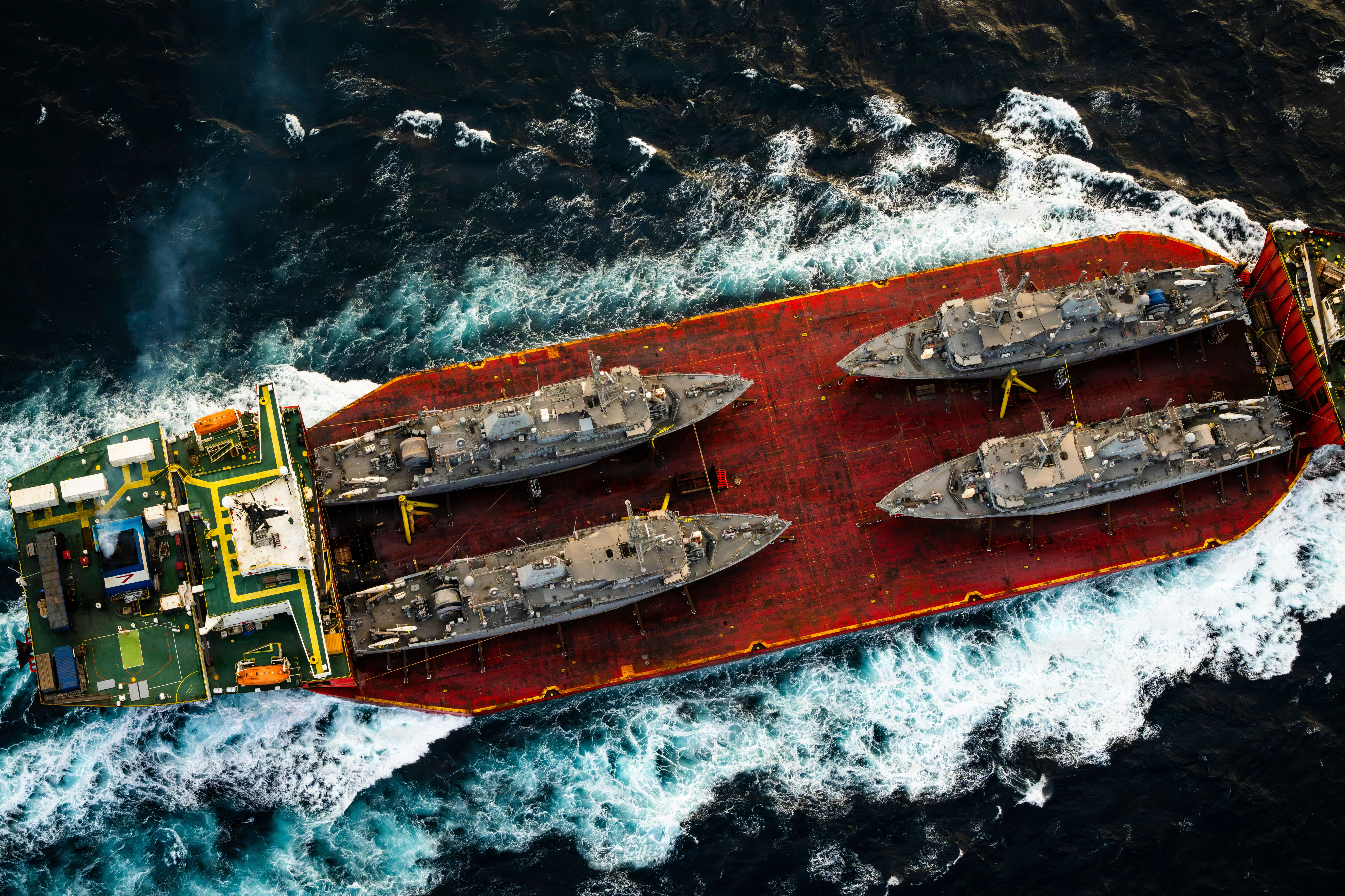 Four US Avenger-class ships sit on the hull of a large ship-transporting vessel.