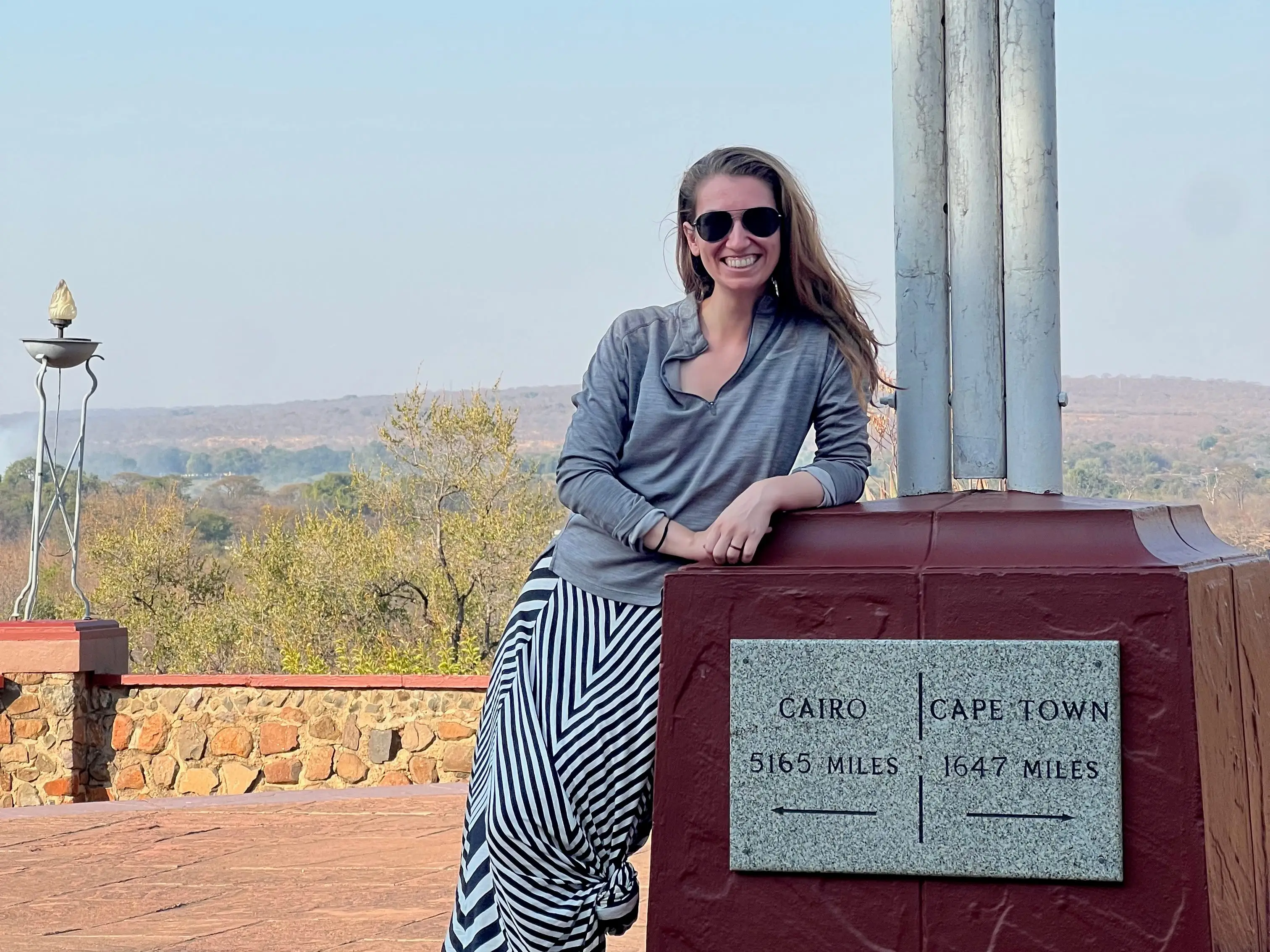 A woman wearing sunglasses is posing next to a sign for Cairo and Cape Town.