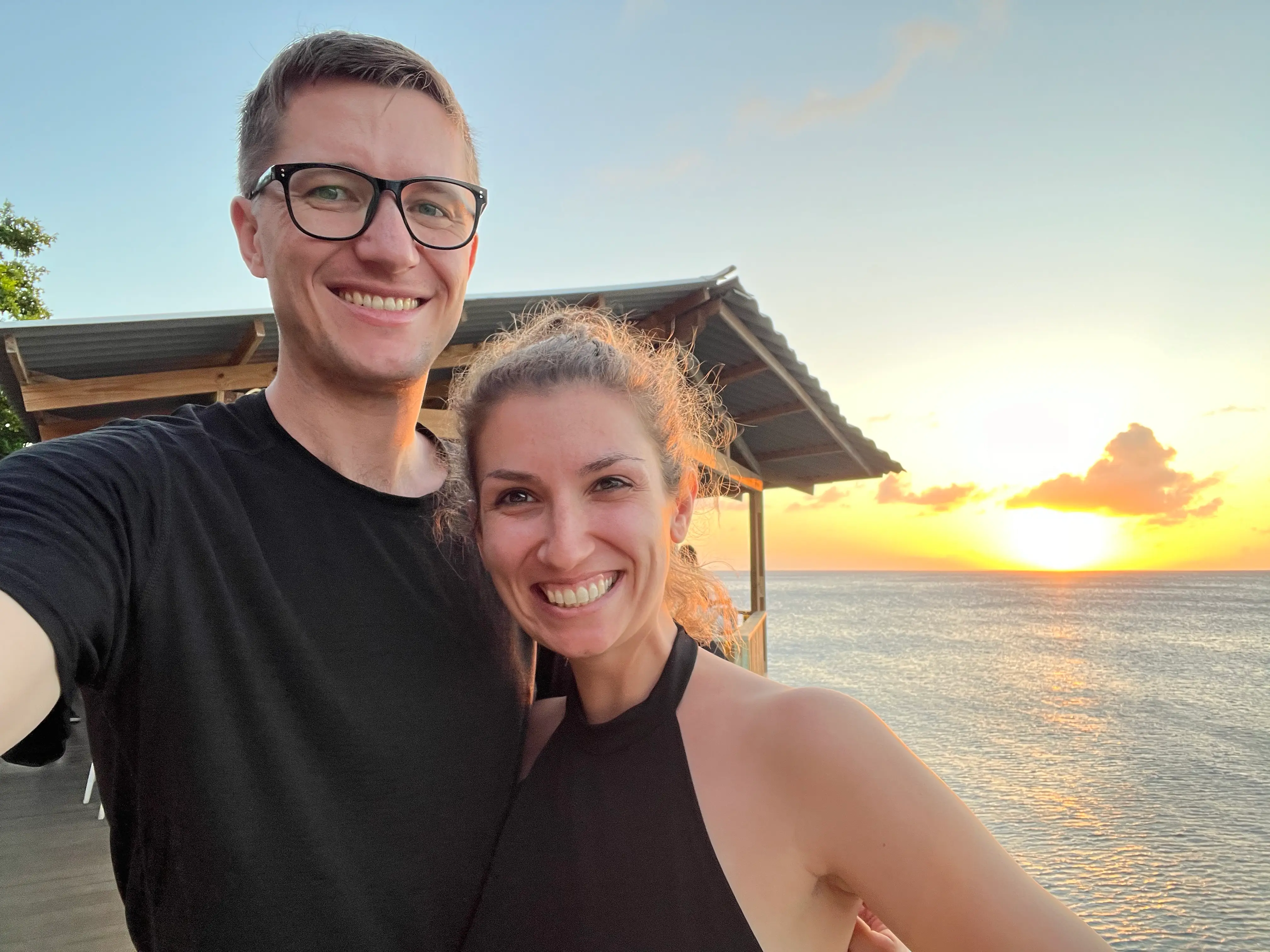 A couple taking a selfie with the sunsetting in the Caribbean as the background.