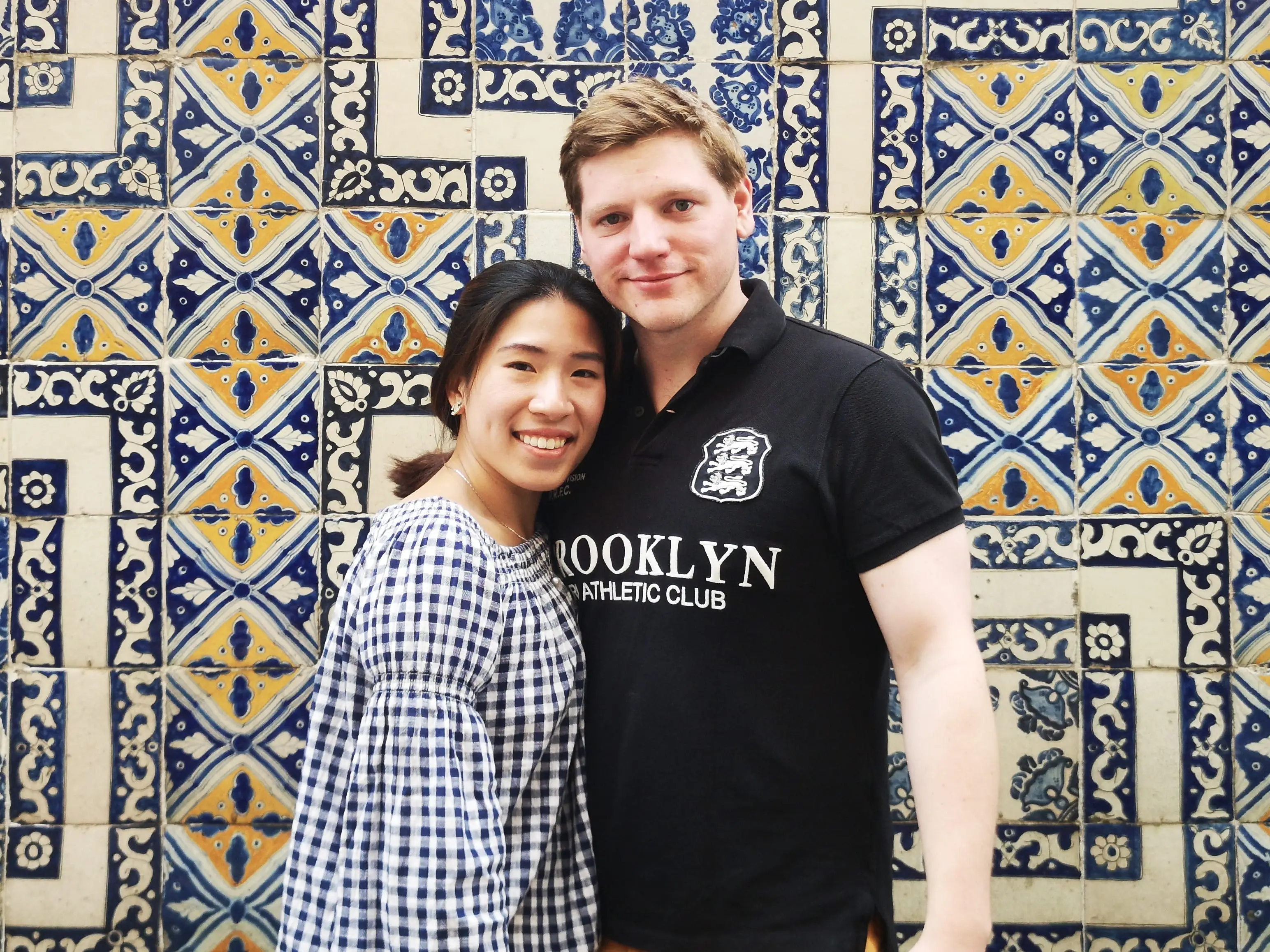 A man and a woman posing in front of a colorful mosaic.