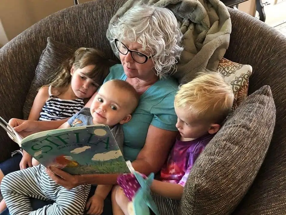 A senior reading to three children in an armchair.