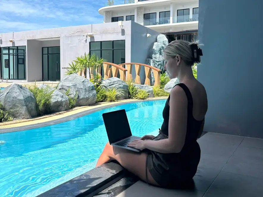 Sally seaton on her laptop while sitting on the edge of a pool