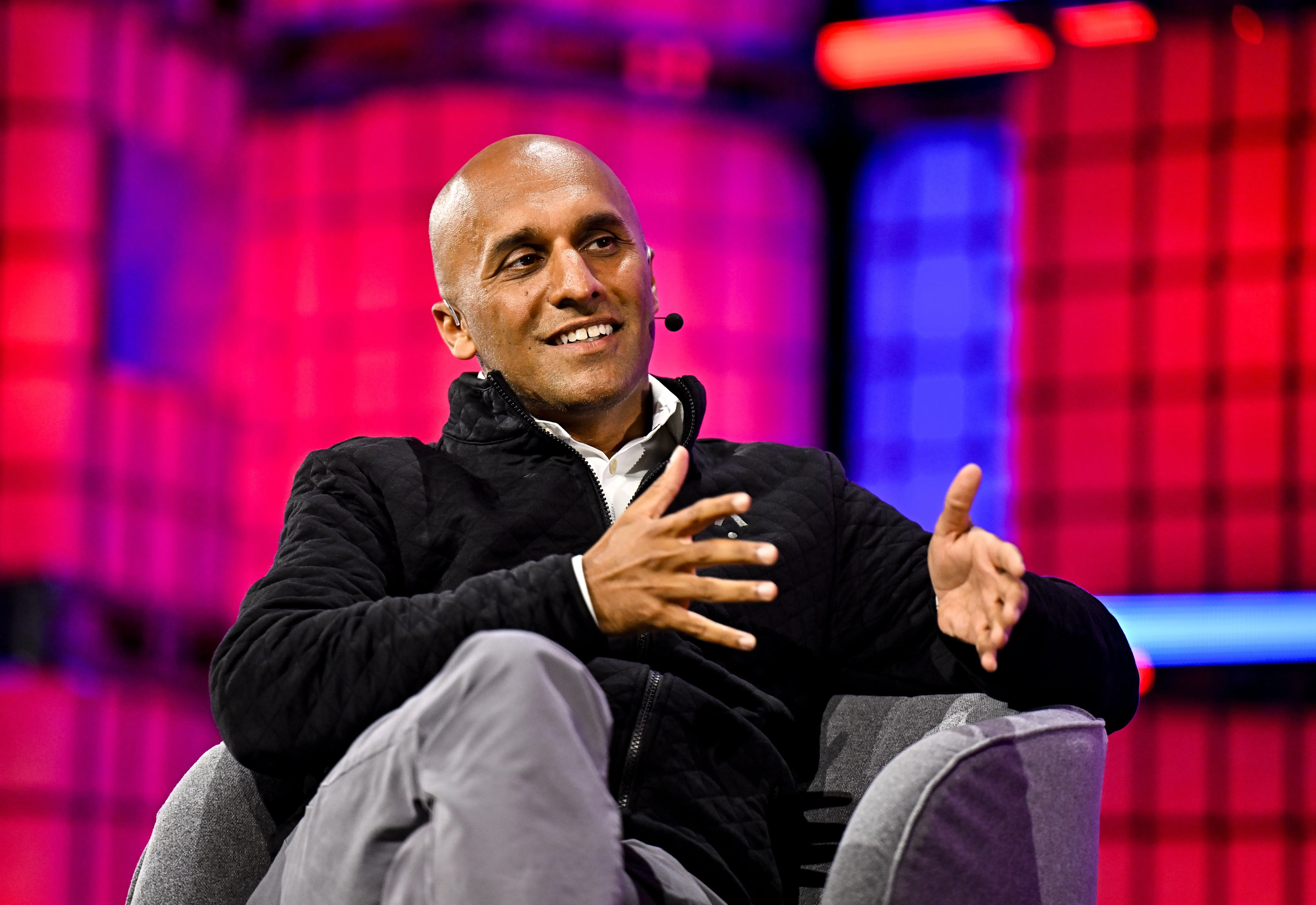 Qasar Younis, the CEO of Applied Intuition, sits on a gray chair onstage. He's wearing a black sweater over a white shirt.