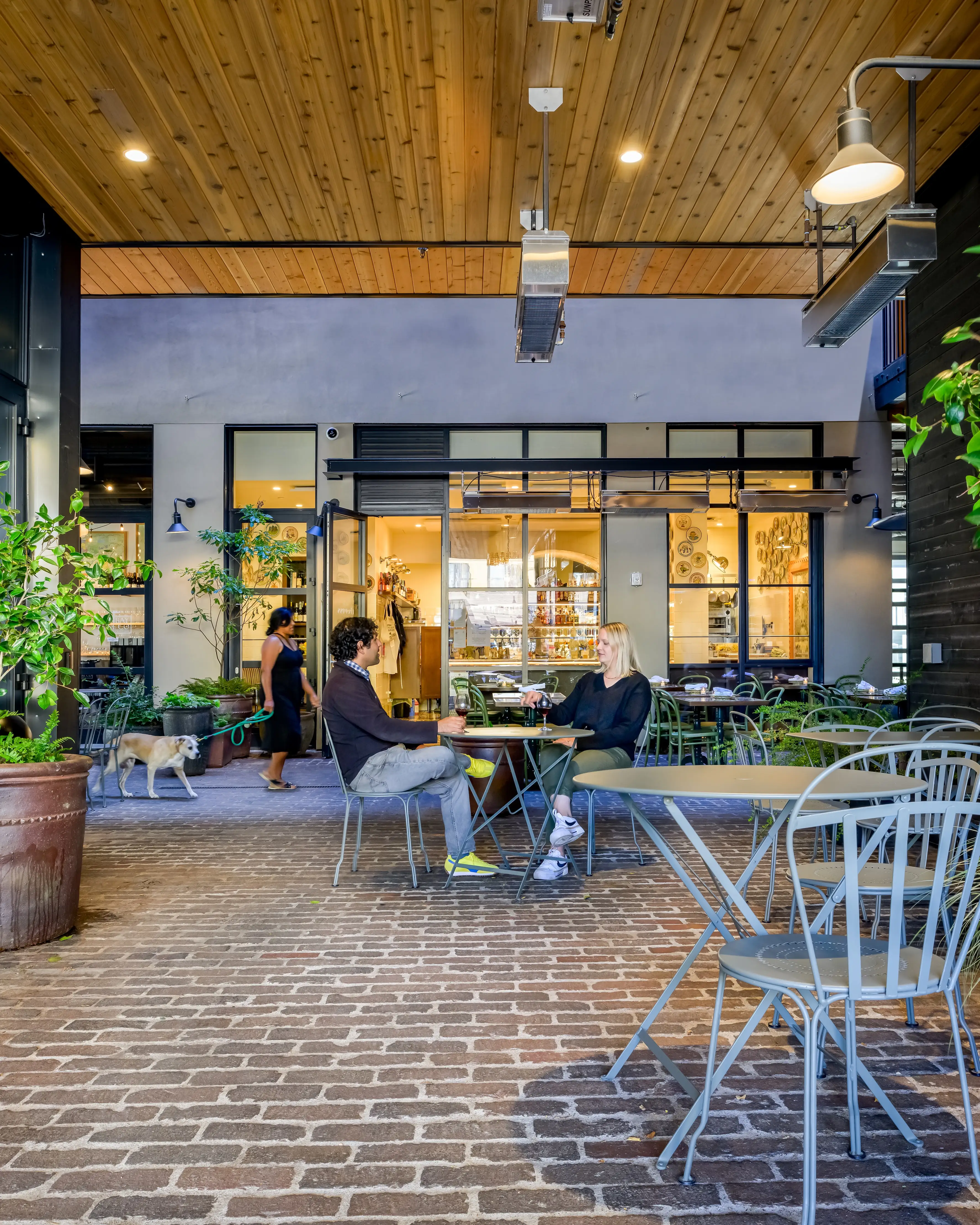A woman walks a dog, and a man and a woman sit down at a table.