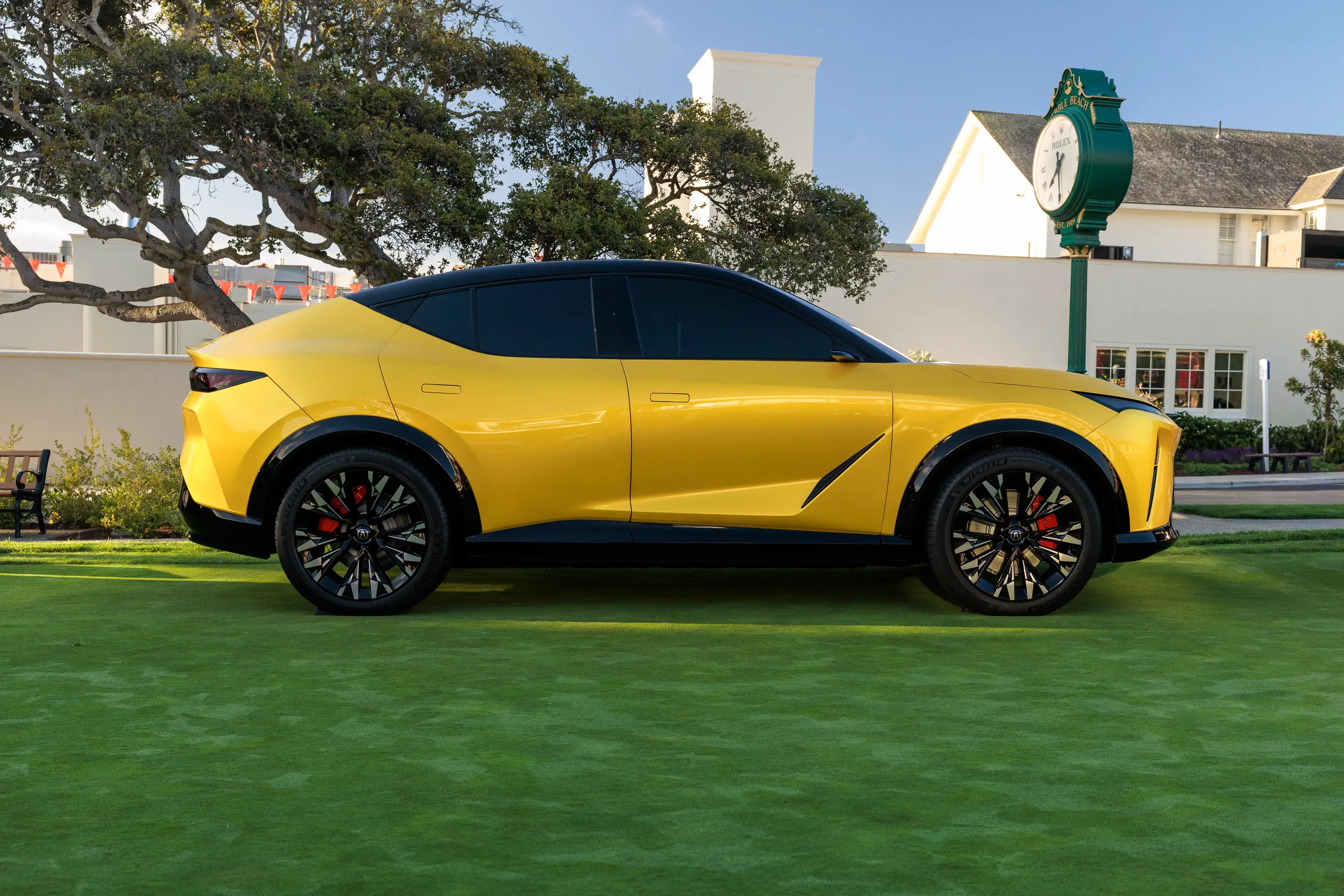 A yellow Acura RSX EV with a black roof and black wheels sits on a well-manicured lawn.