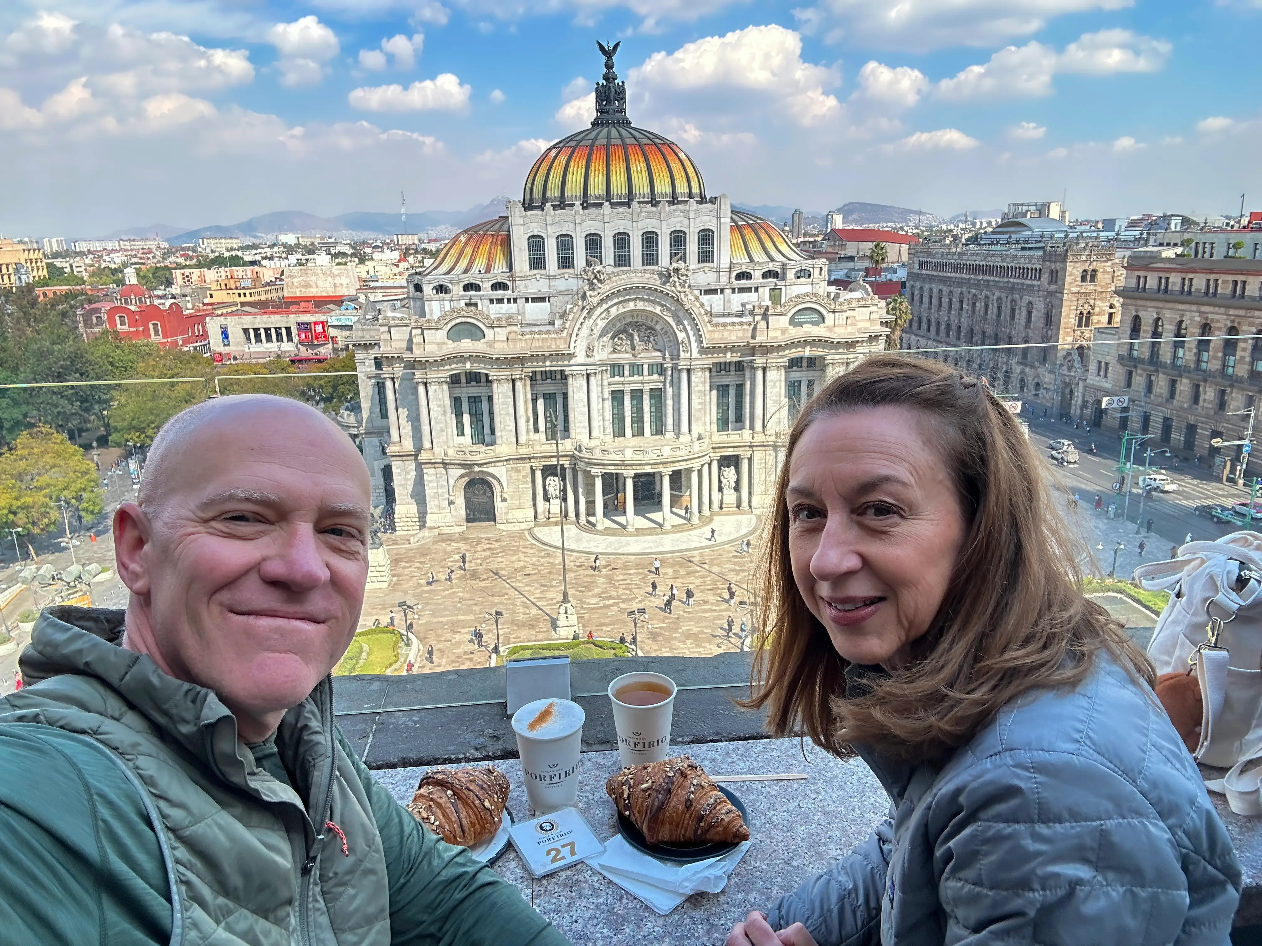 Tom and his wife sit at a table with coffee and pastries, overlooking Palacio de Bellas Artes.