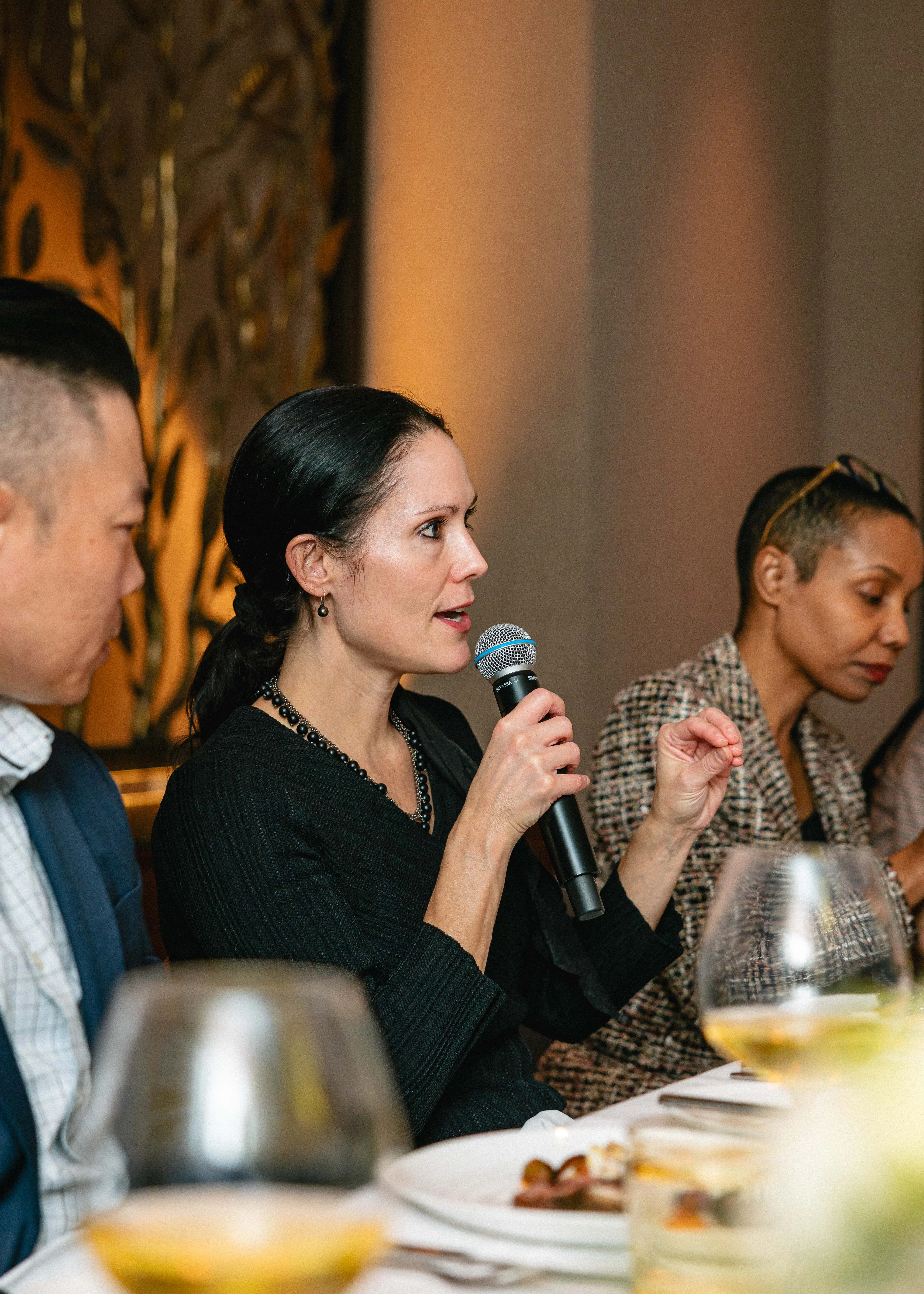 Profile view of woman at formal dinner speaking into a microphone.