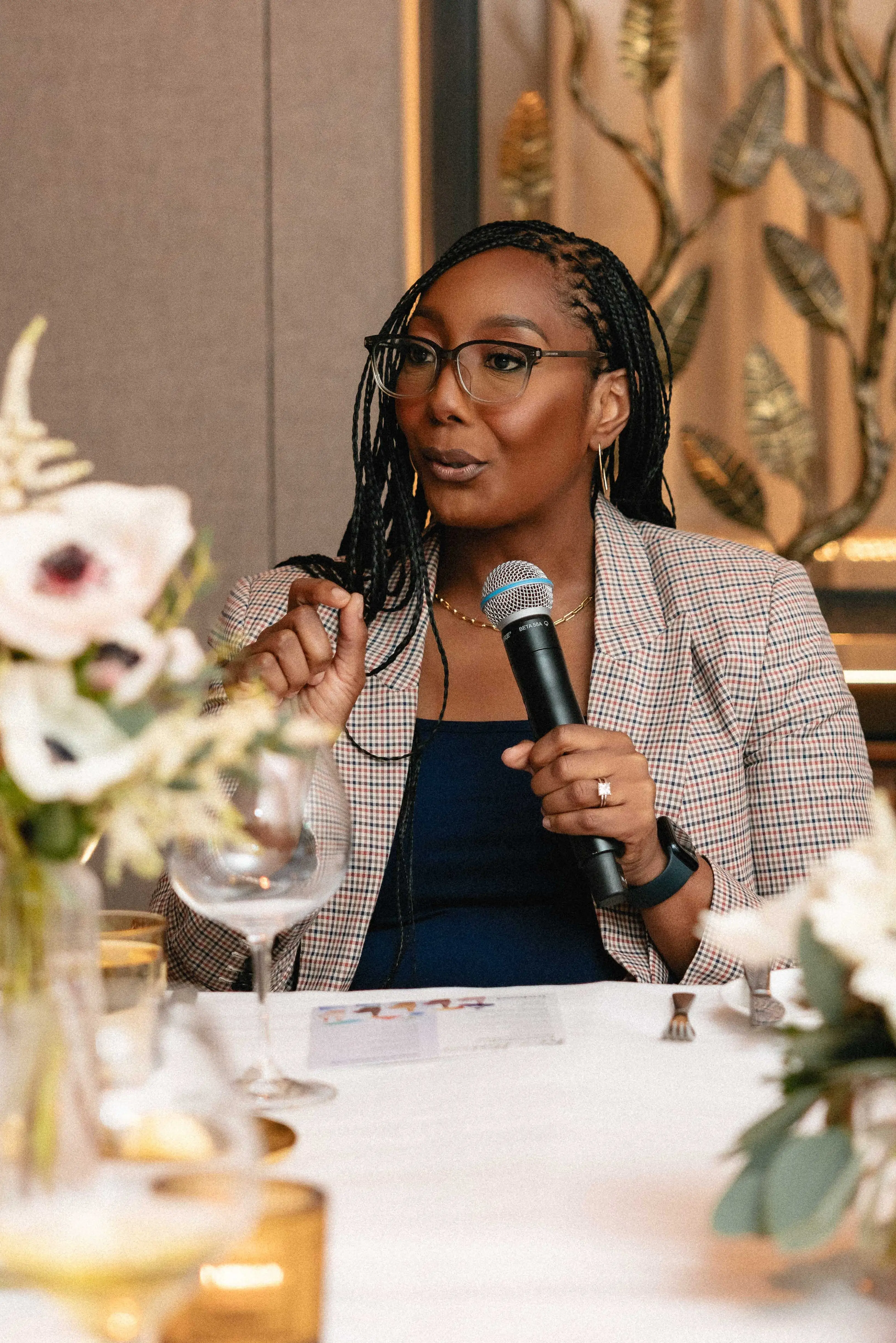 Black woman with glasses speaking into a microphone at a formal dinner