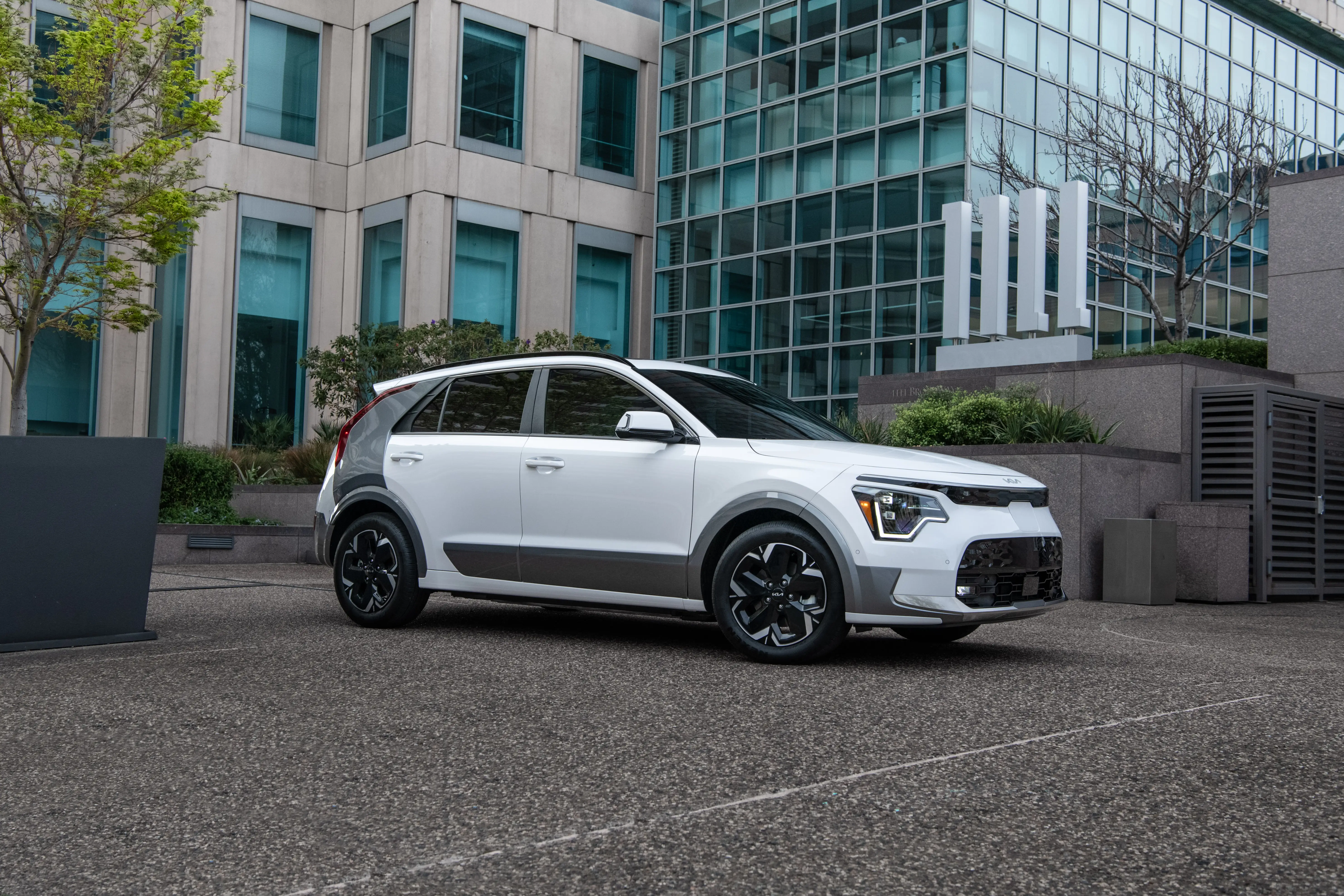 A white Kia Niro EV, with a silver-painted c-pillar, is parked with its wheels turning toward the driver's side.