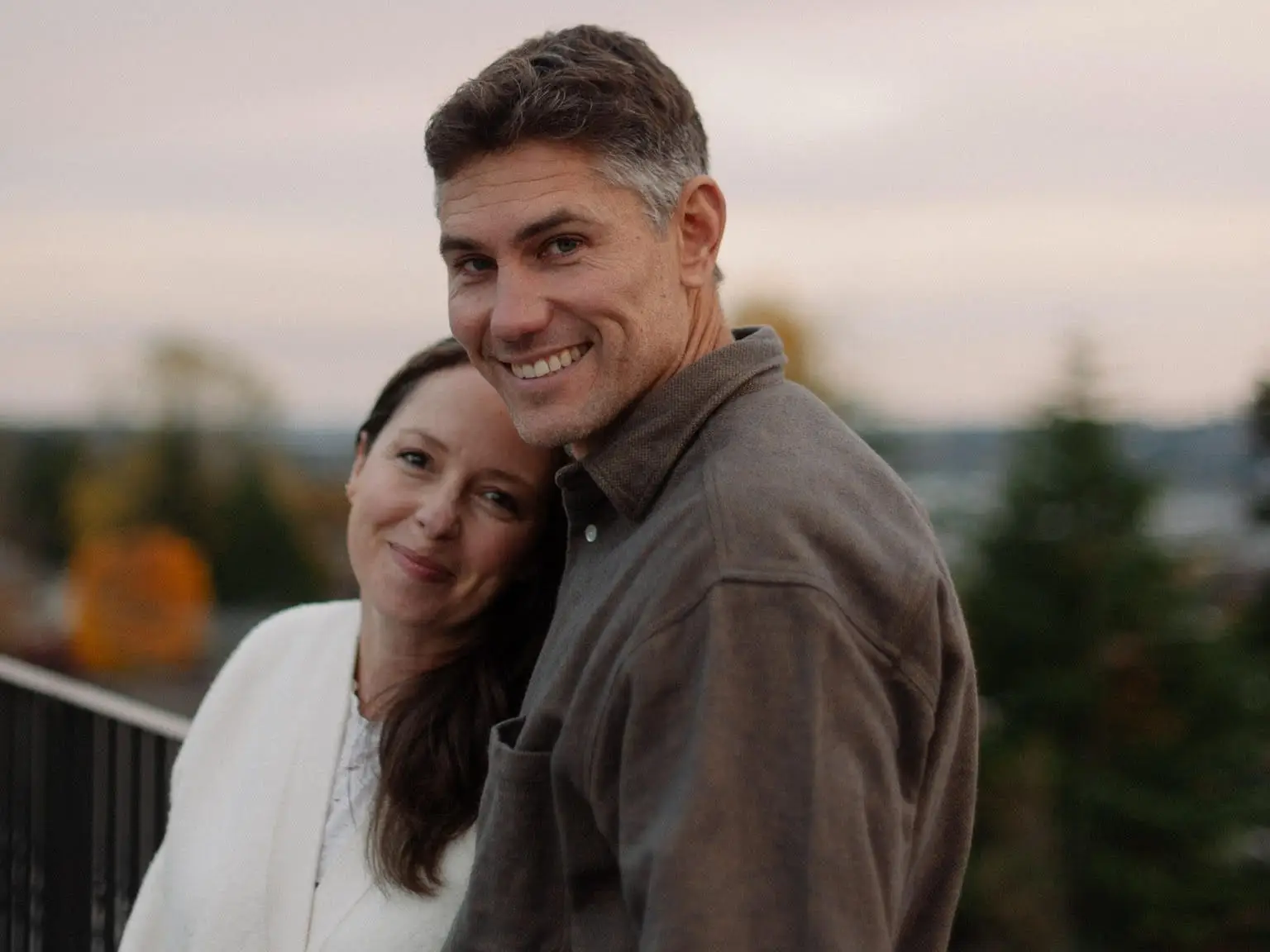 A man and a woman smile on a balcony.