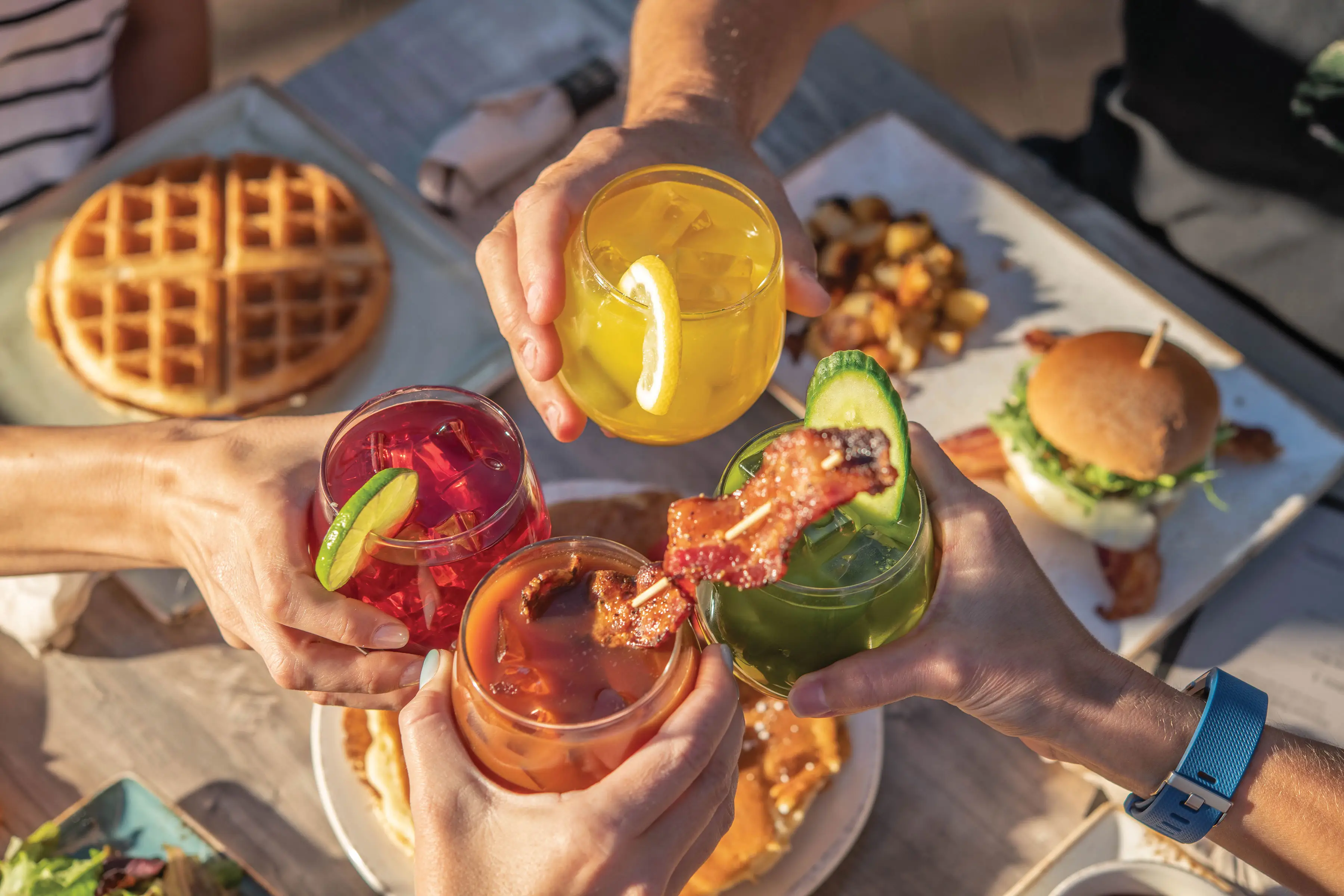 Four cocktail glasses meet to cheers in the center of a brunch table.