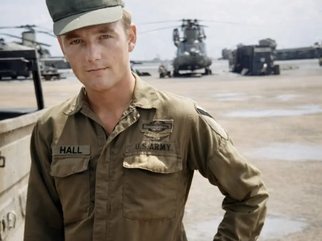 A soldier in the US Army with military helicopters behind him.