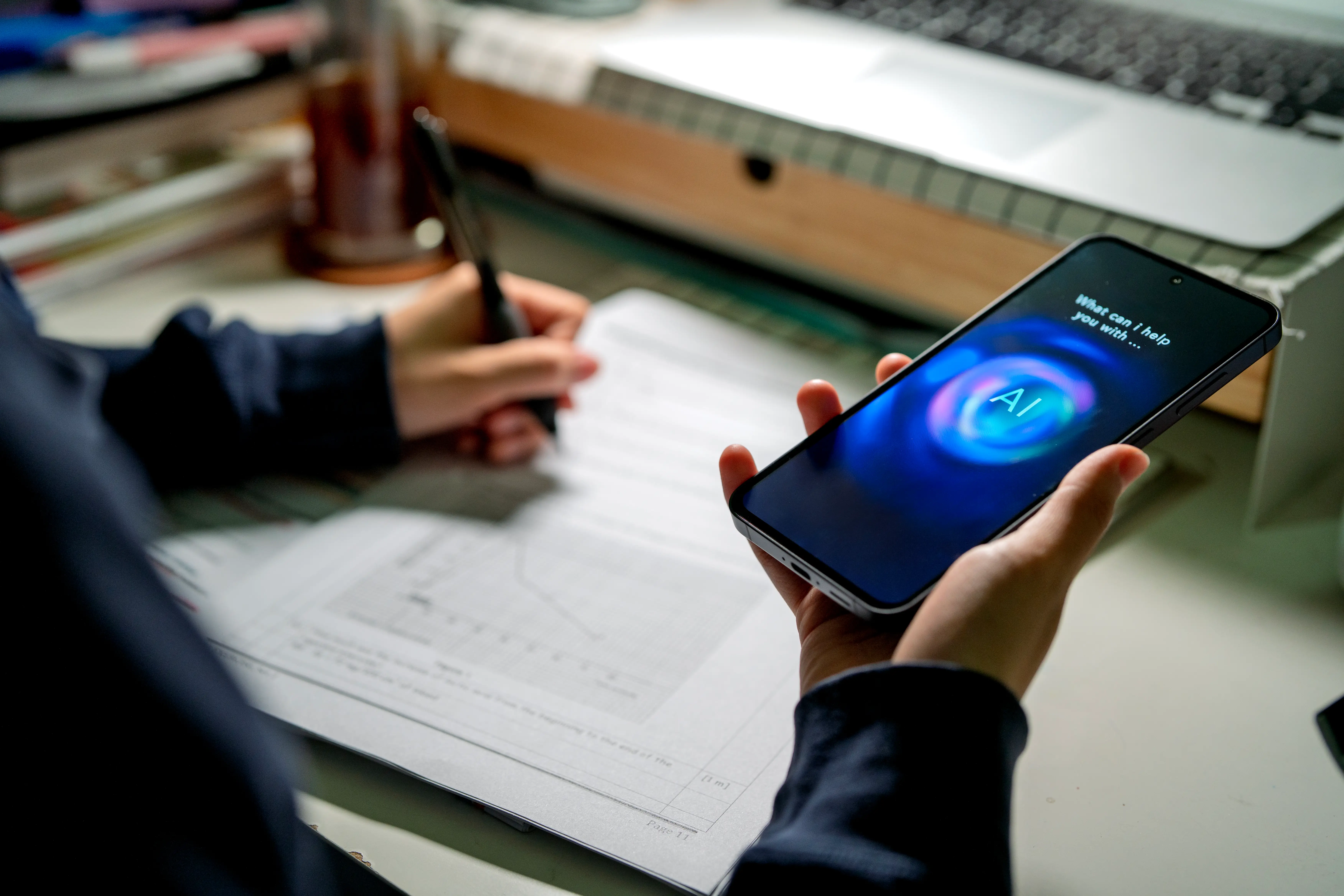 A young person holds a smart phone while doing homework.