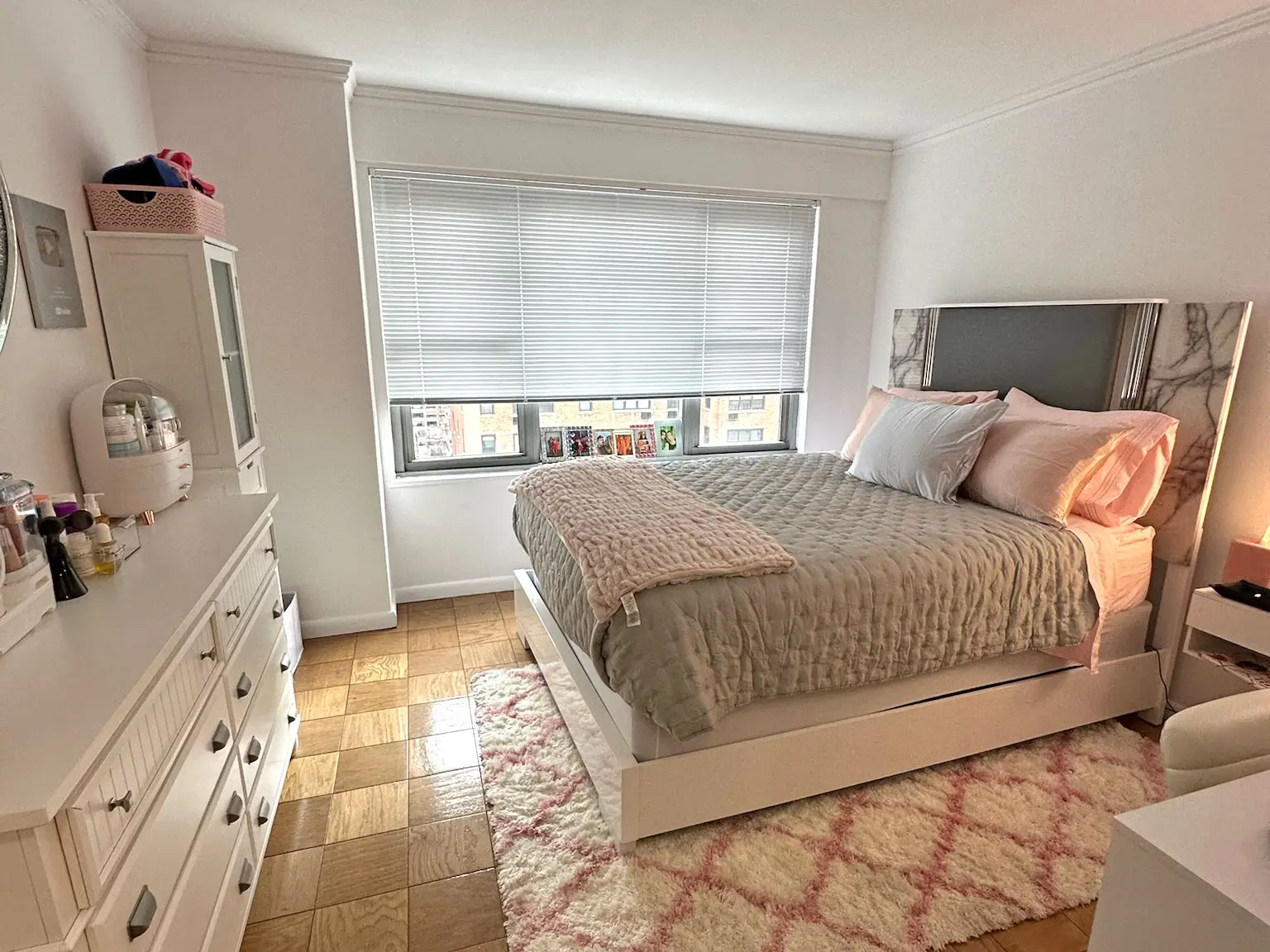 A bedroom with gray and pink bedding and white furniture.