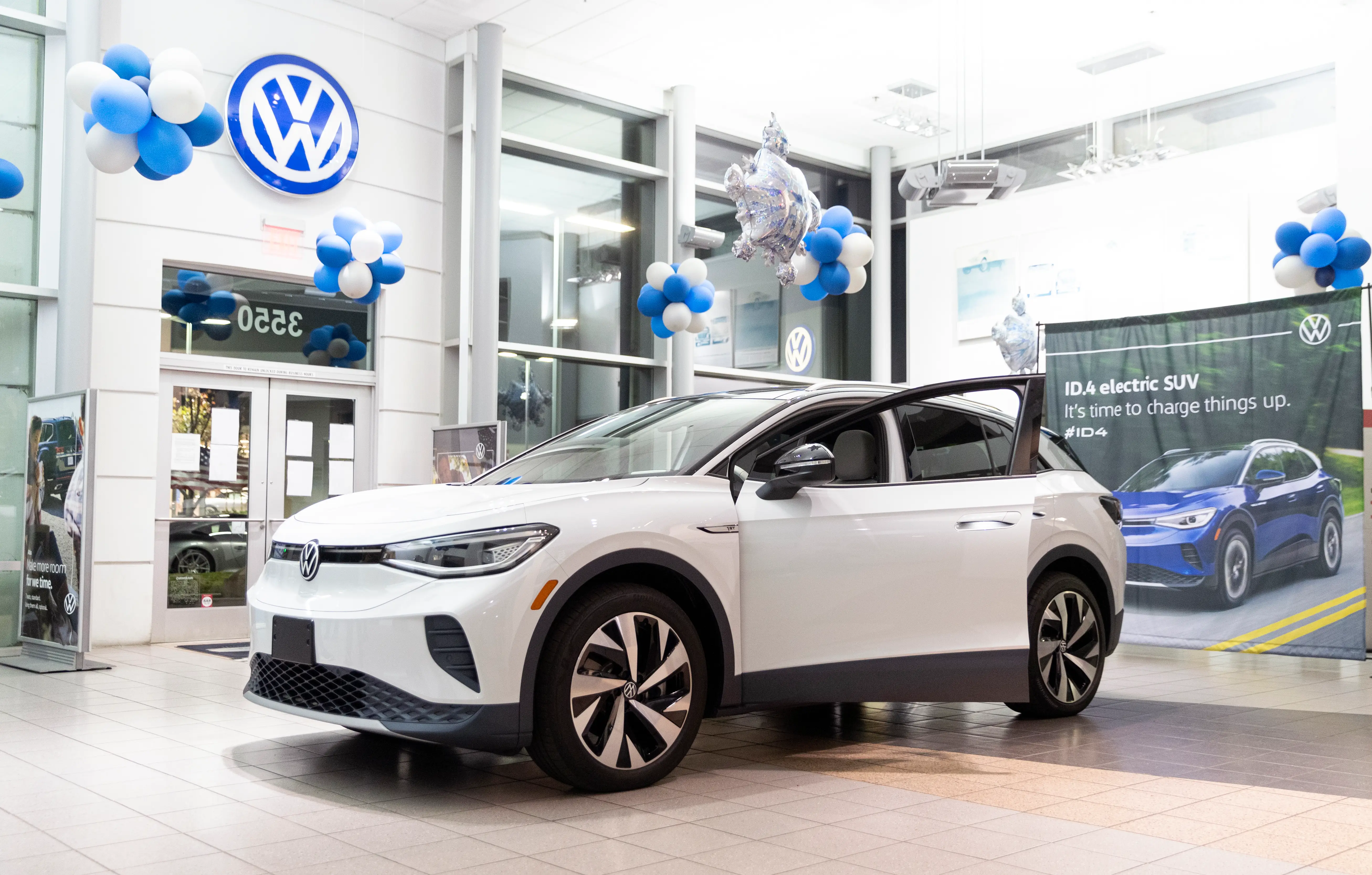 A white Volkswagen ID. 4 with its driver's door is parked inside a VW dealership showroom.