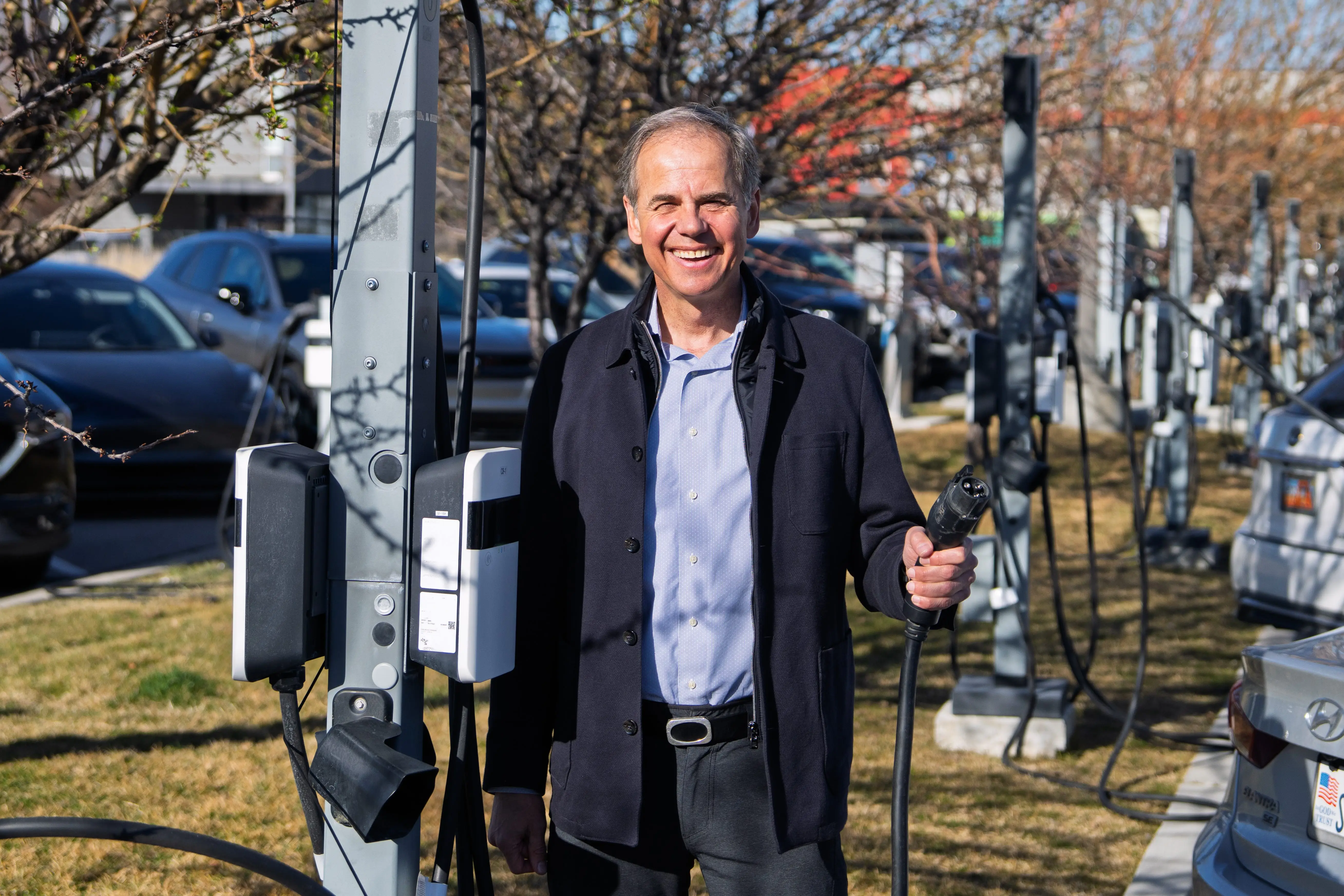 A man in a parking lot holds an electric vehicle charging plug.