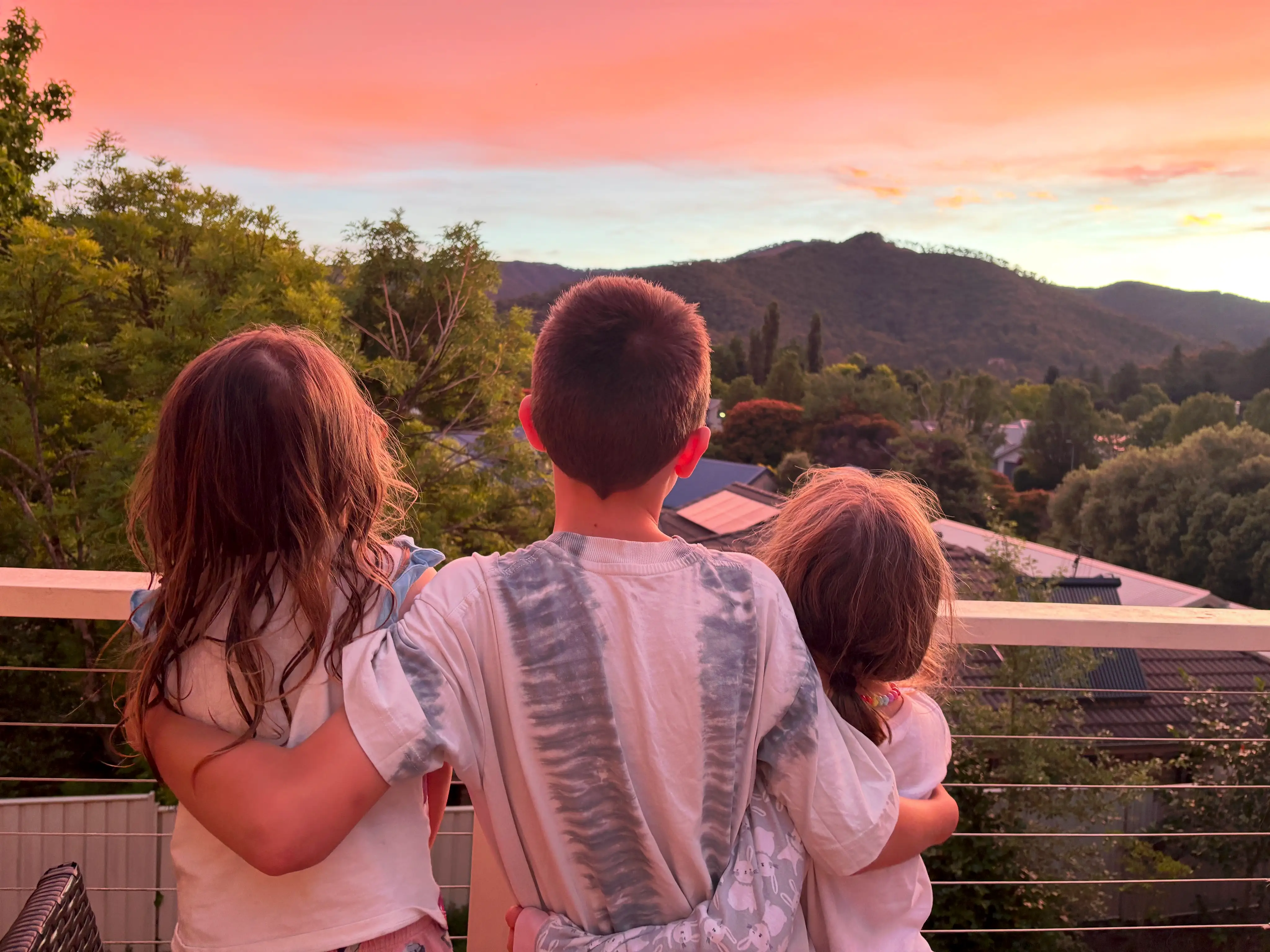 Three kids staring at sunset over mountains/trees