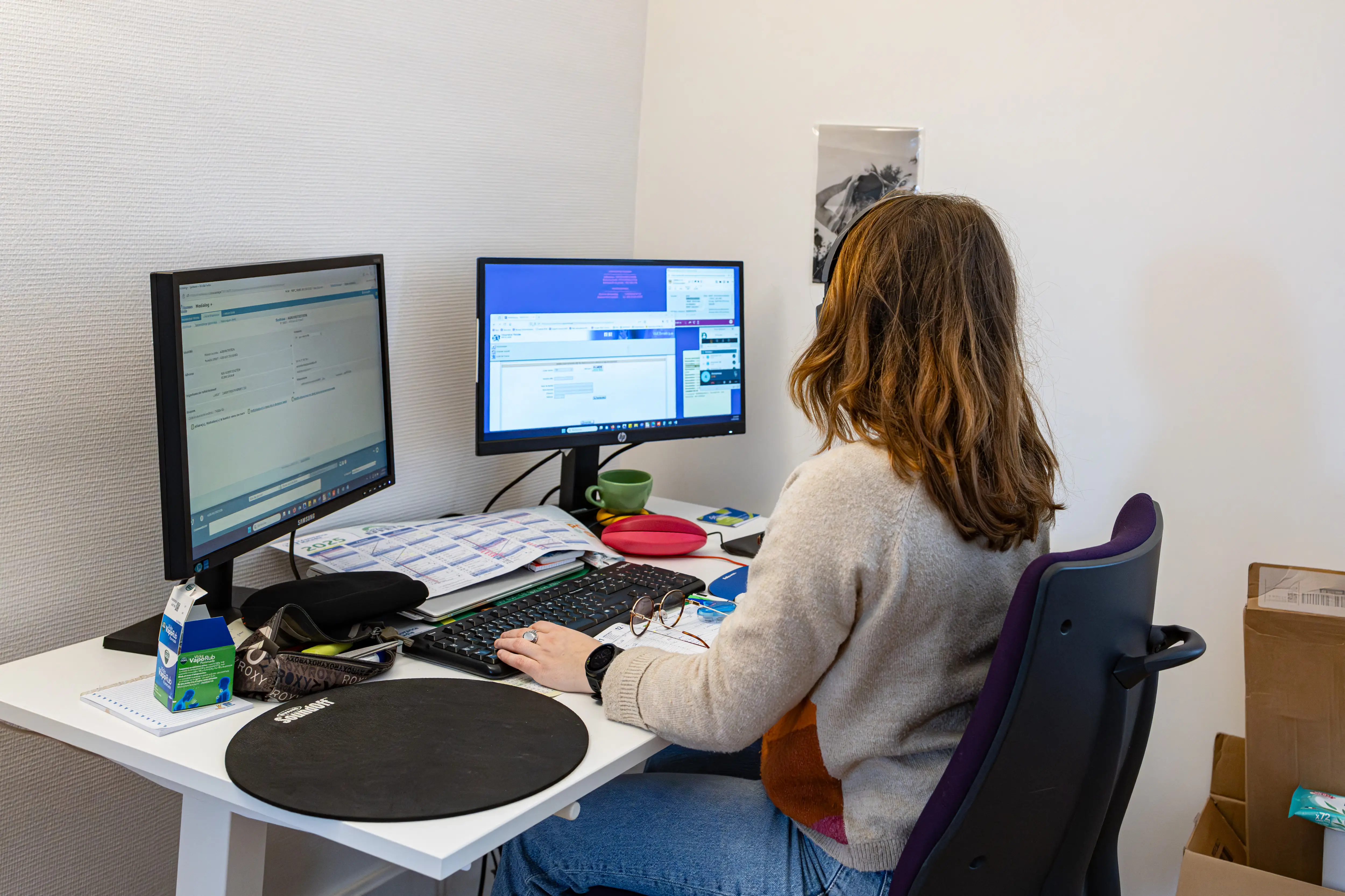 A woman works at a desk with dual monitors