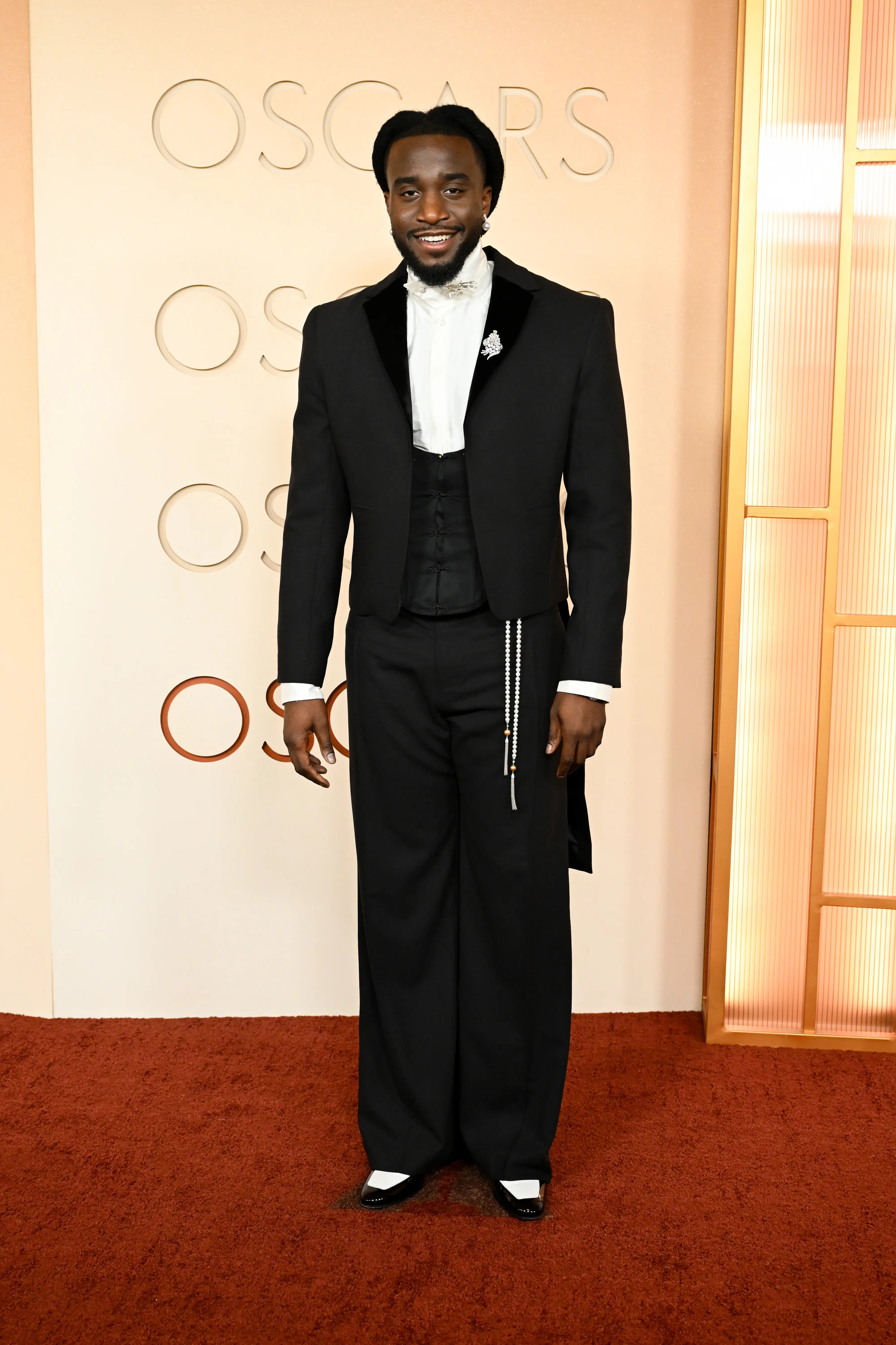 Shaboozey walks the Oscars red carpet in a black suit.