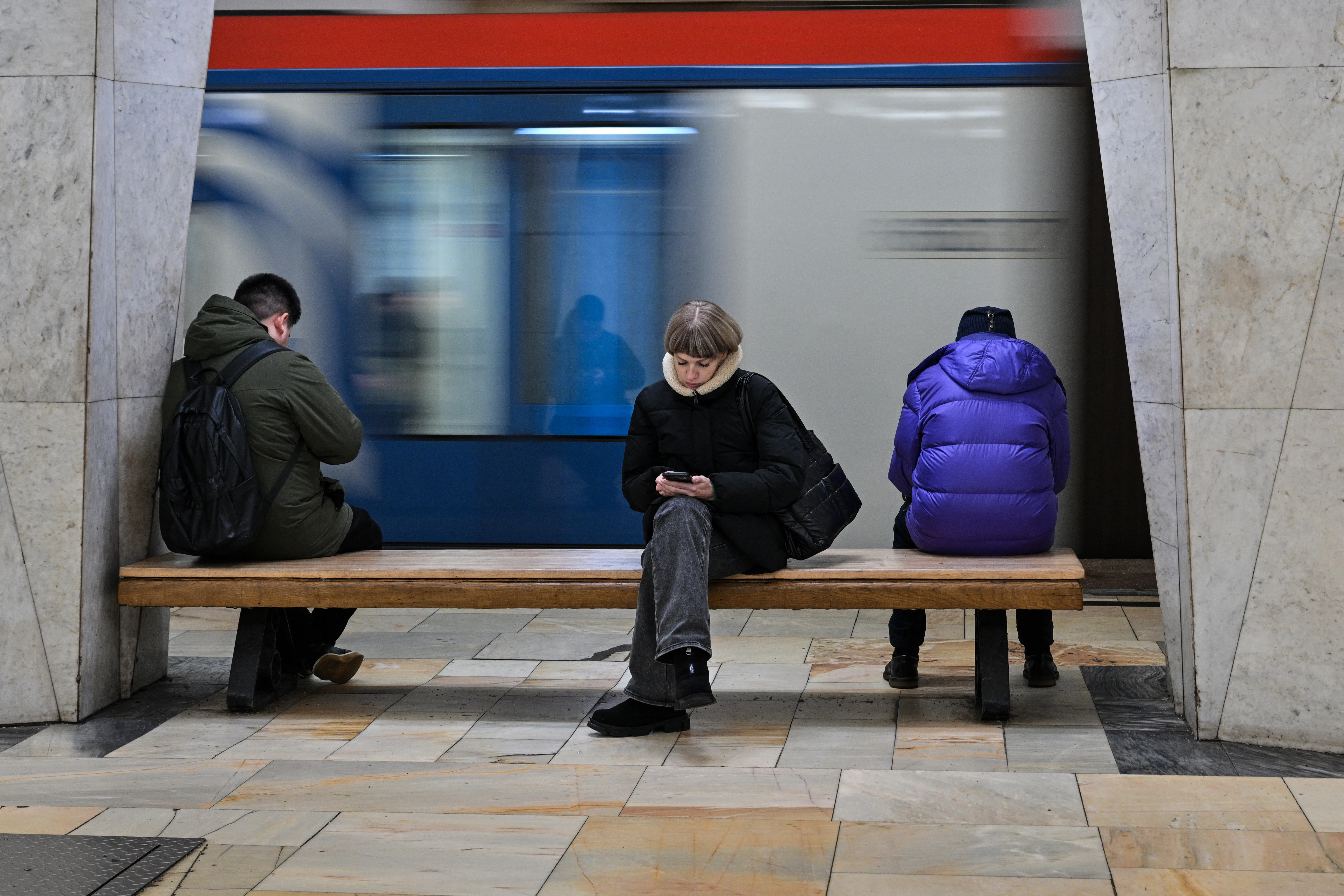 People use their smartphones while sitting on a bench at a metro station in Moscow on Feb. 12, 2026.