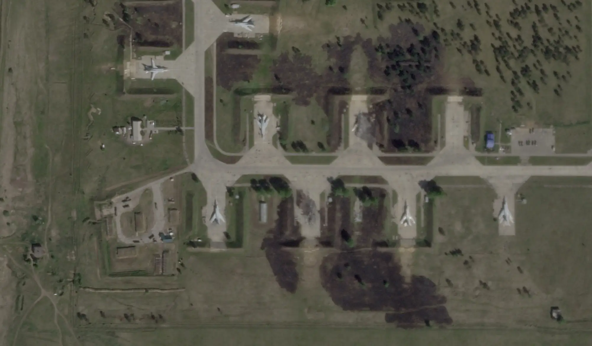 A satellite image shows multiple planes sitting at a base and large black scorch marks