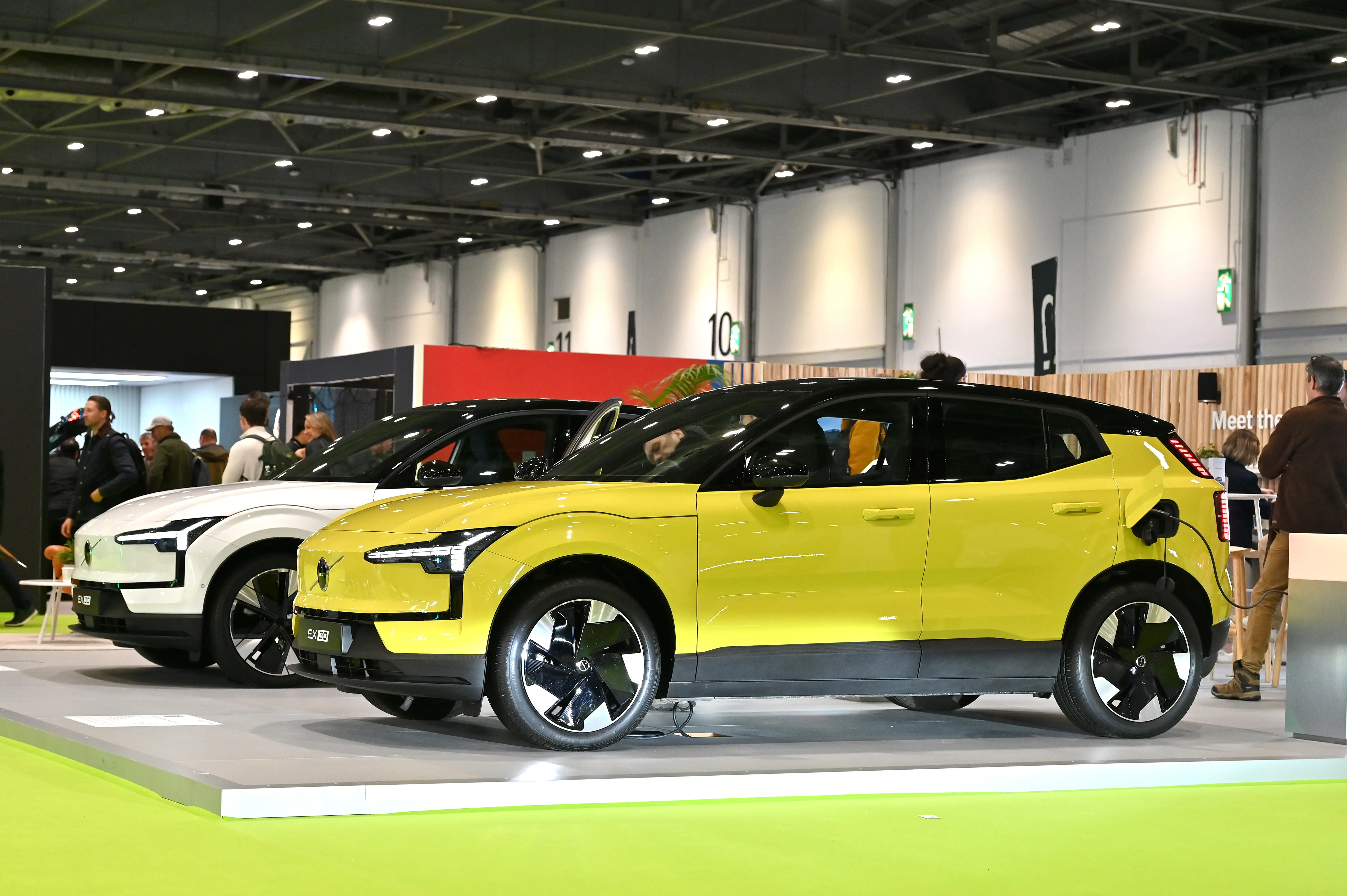 Two Volvo EX30s - one is bright yellow, and the other is white - are parked next to each other in a showroom during an expo.