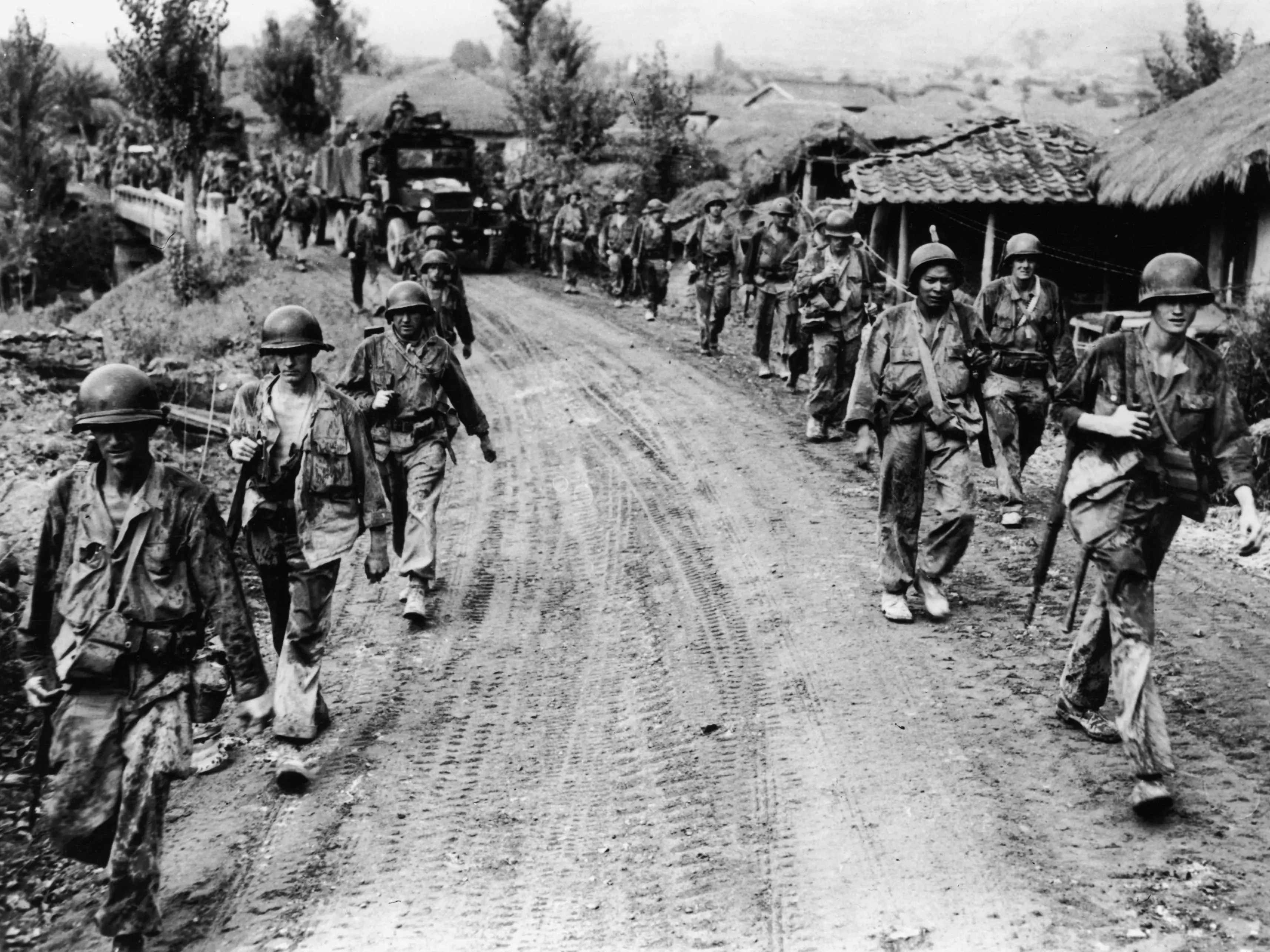 American soldiers walking in two lines on the side of a dirt road.