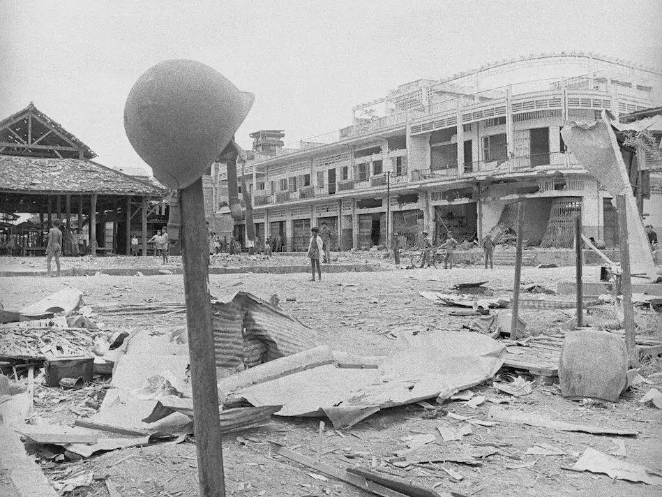 A US Army helmet sits on a pole in front of rubble.