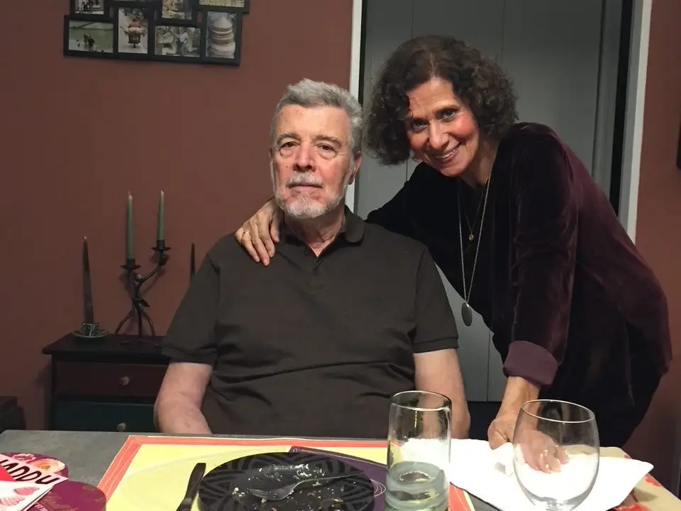 A man and woman sitting and standing at a dinner table.