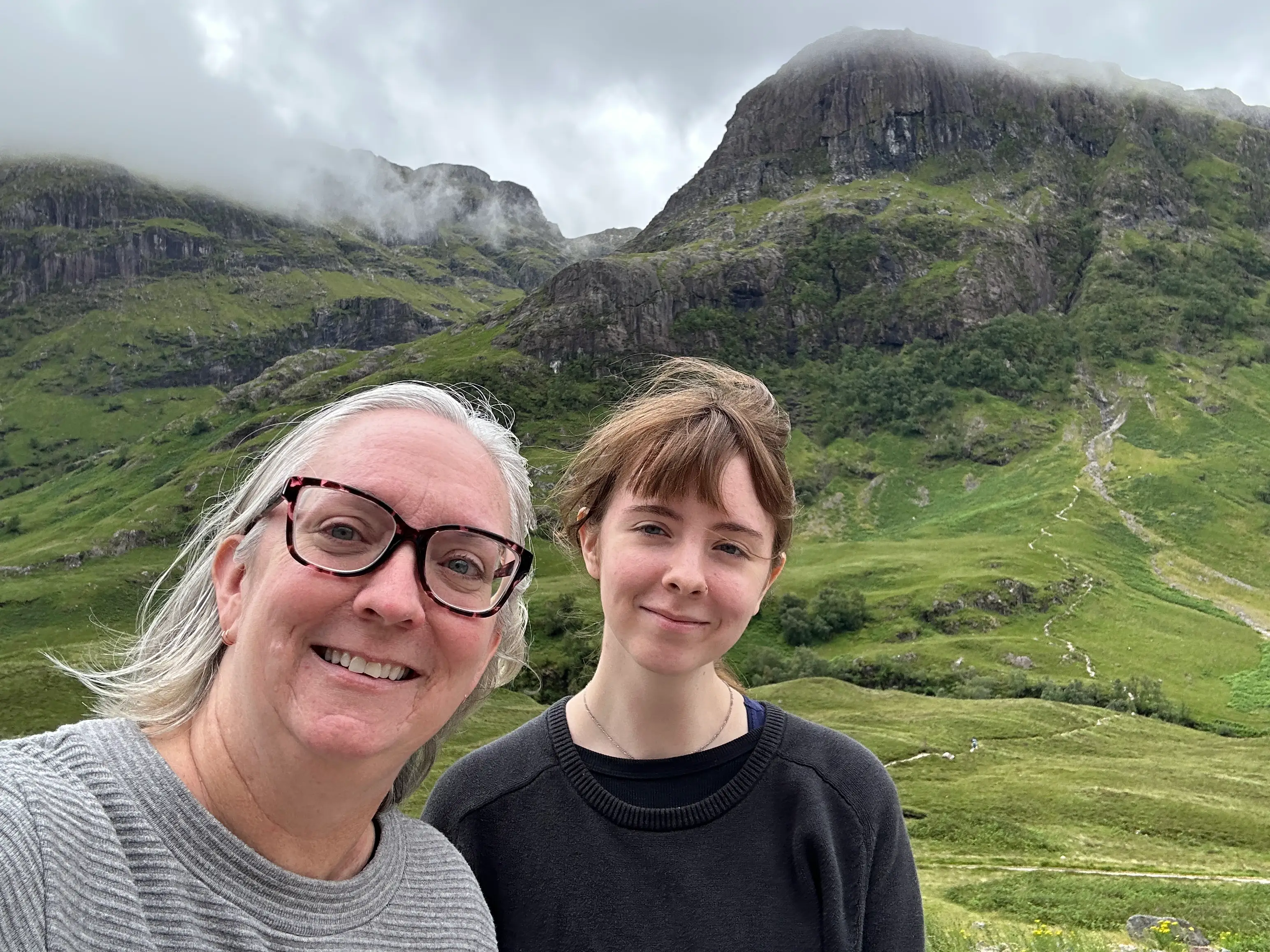 The aunther and her daughter pose in front of green mountains.