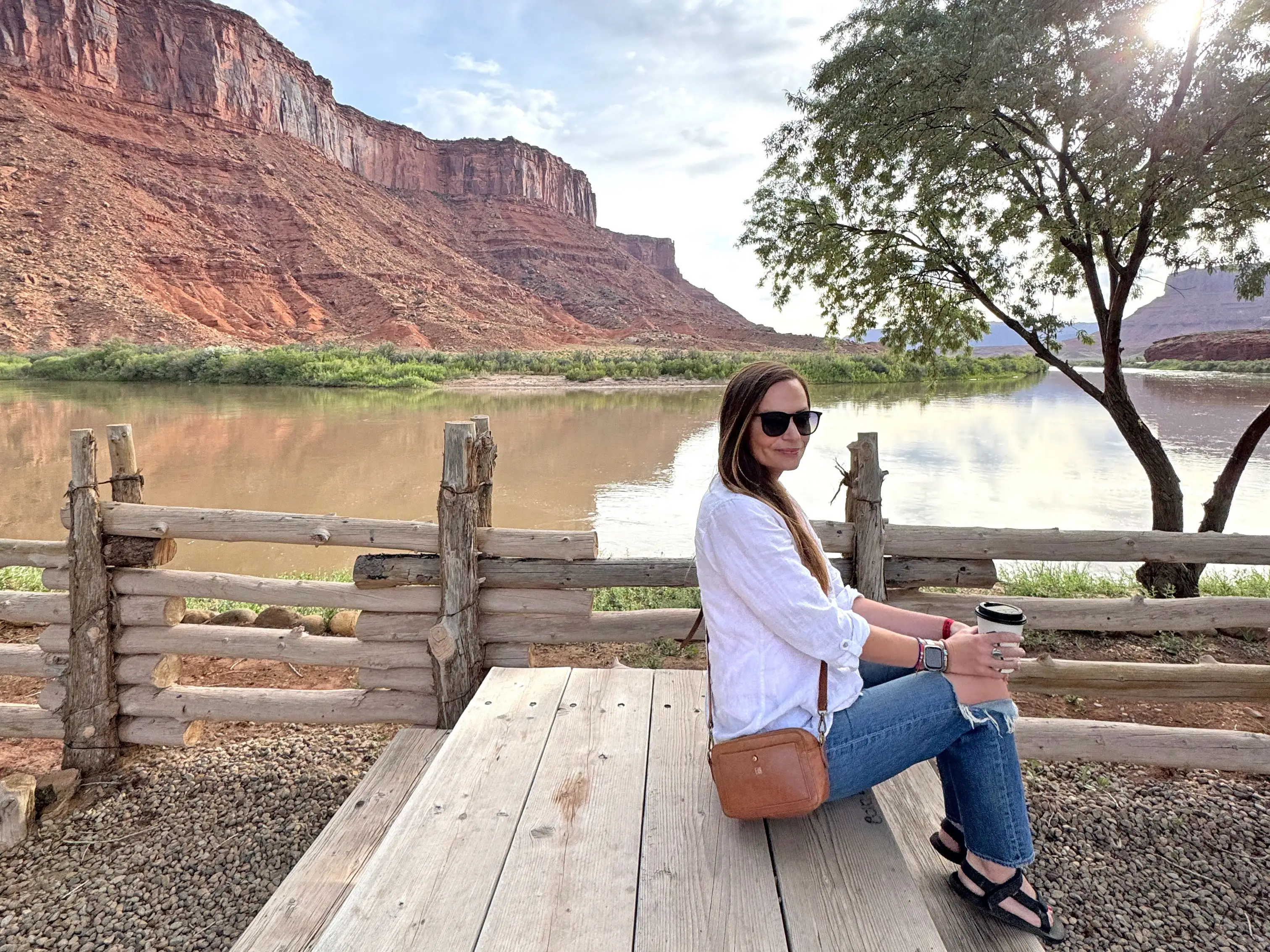 Emily sits on a picnic bench with a lake and red-rock formations behind her.