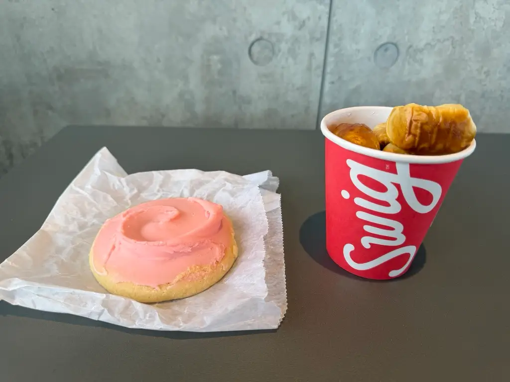 Sugar cookie with pink icing next to Swig cup with pretzel bites inside