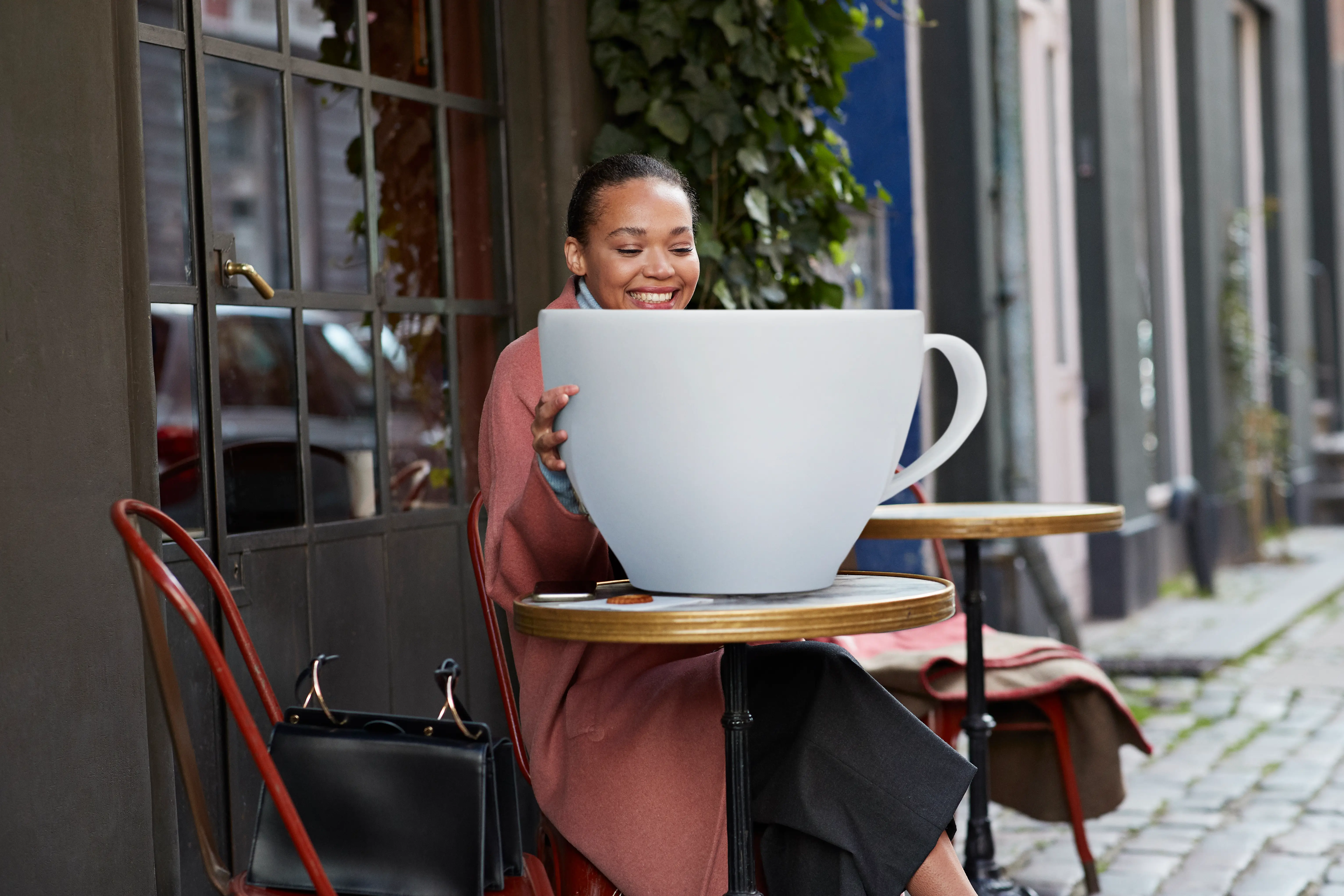 a comically large cup of coffee on a table in front of a cafe