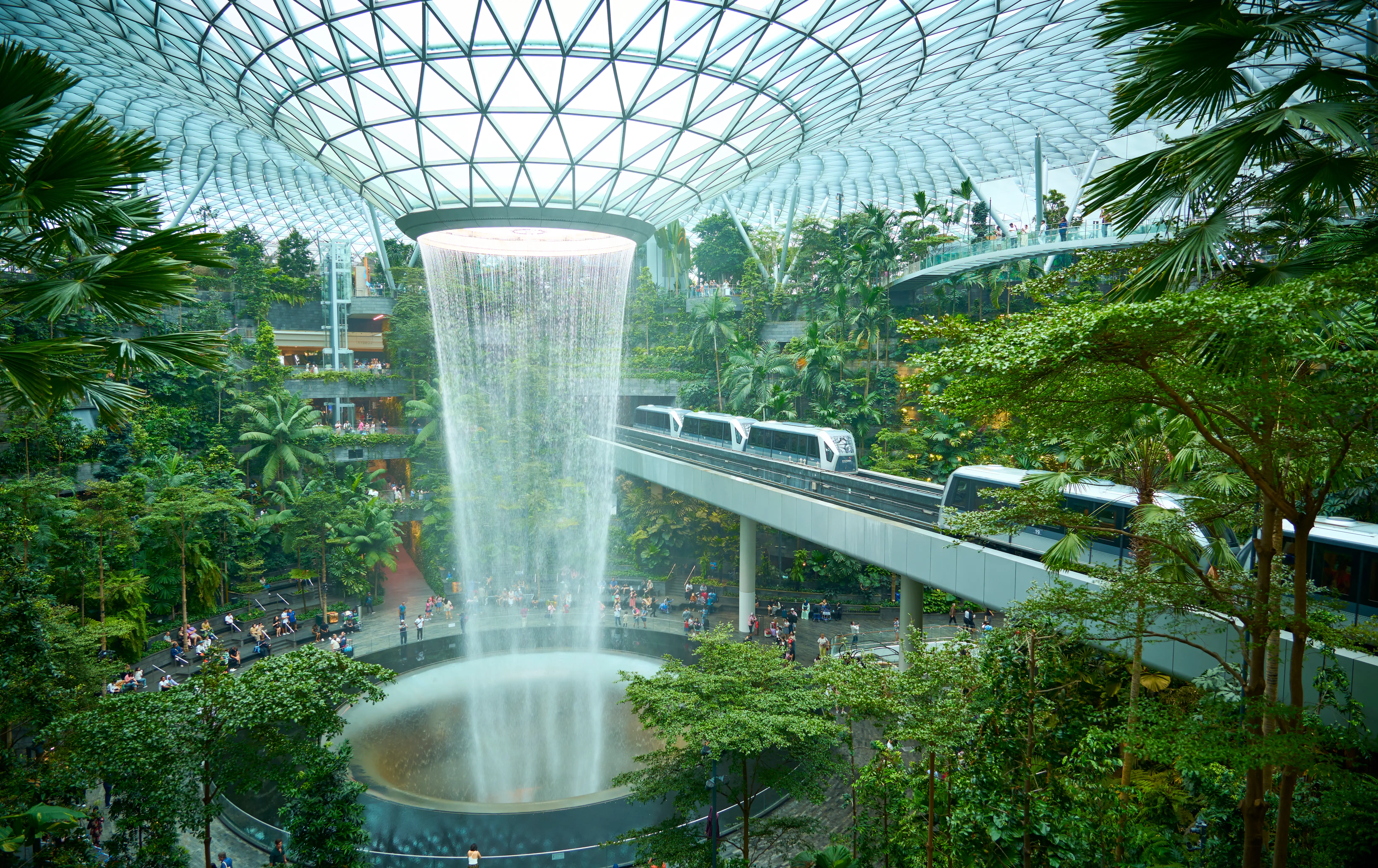 Singapore- Dec, 12, 2024: Futuristic indoor waterfall surrounded by lush vegetation with a skytrain passing by at jewel changi airport, singapore