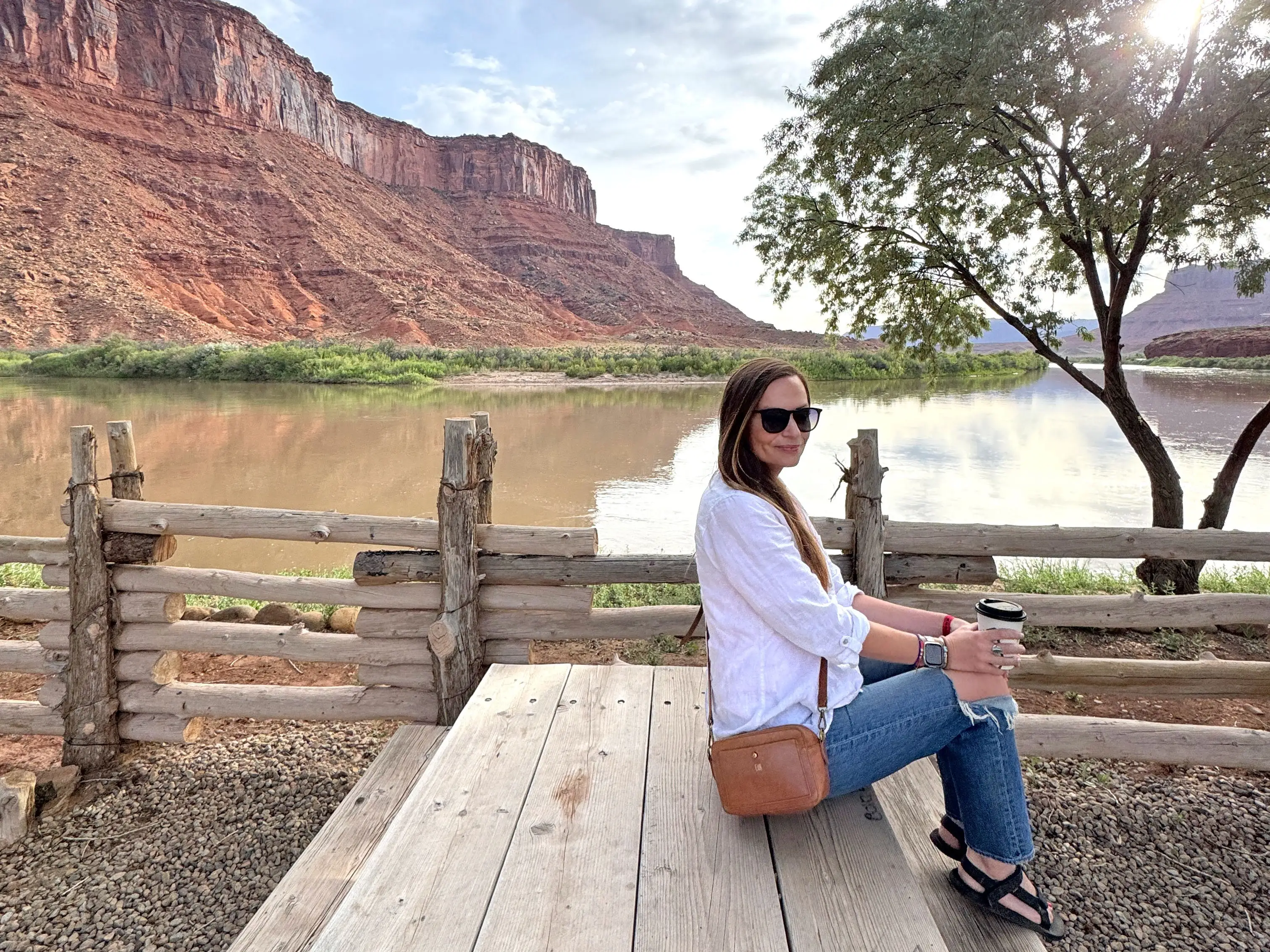 Emily sits on a picnic bench with a lake and red-rock formations behind her.