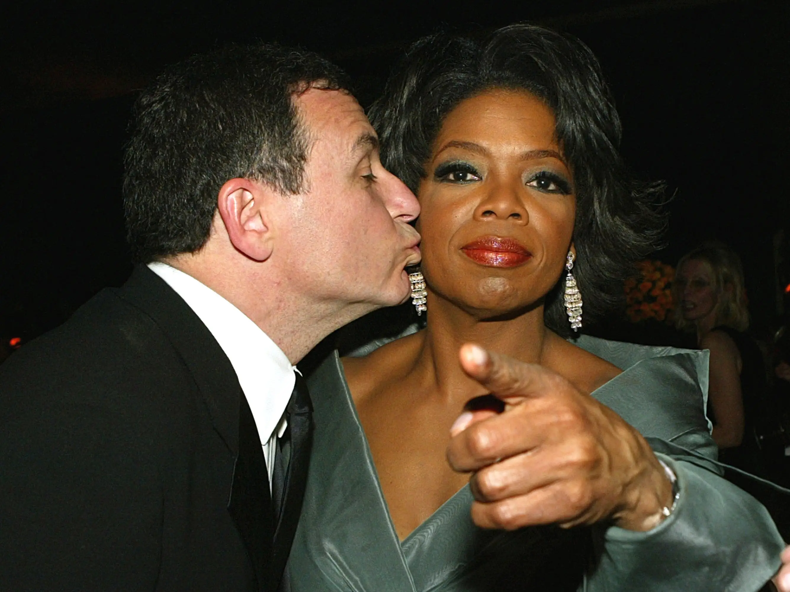 ABC president Bob Iger (L) kisses Oprah Winfrey (R) as she points toward the camera.