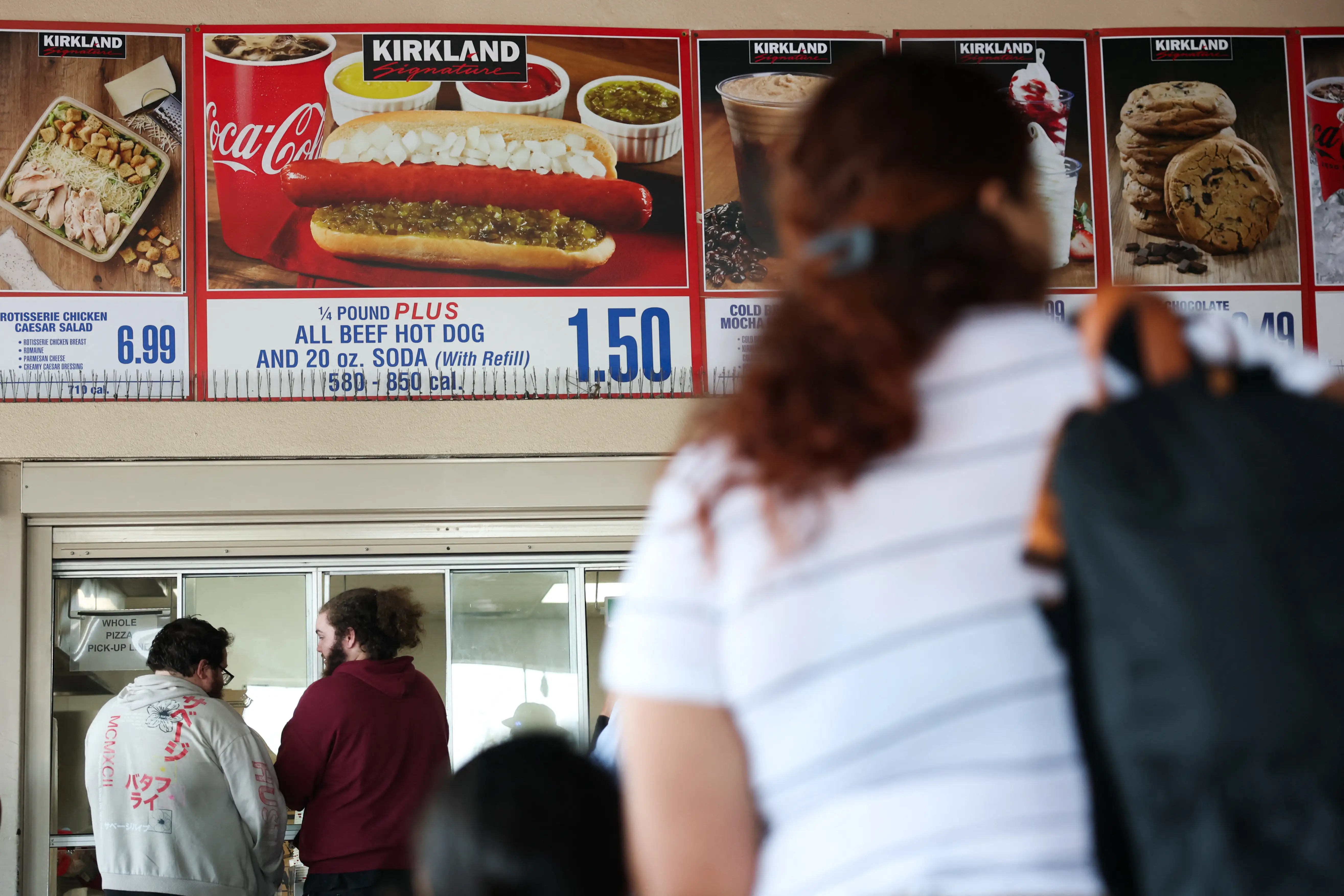 Customers wait in line to order below signage for the Costco Kirkland Signature $1.50 hot dog and soda combo, in California.