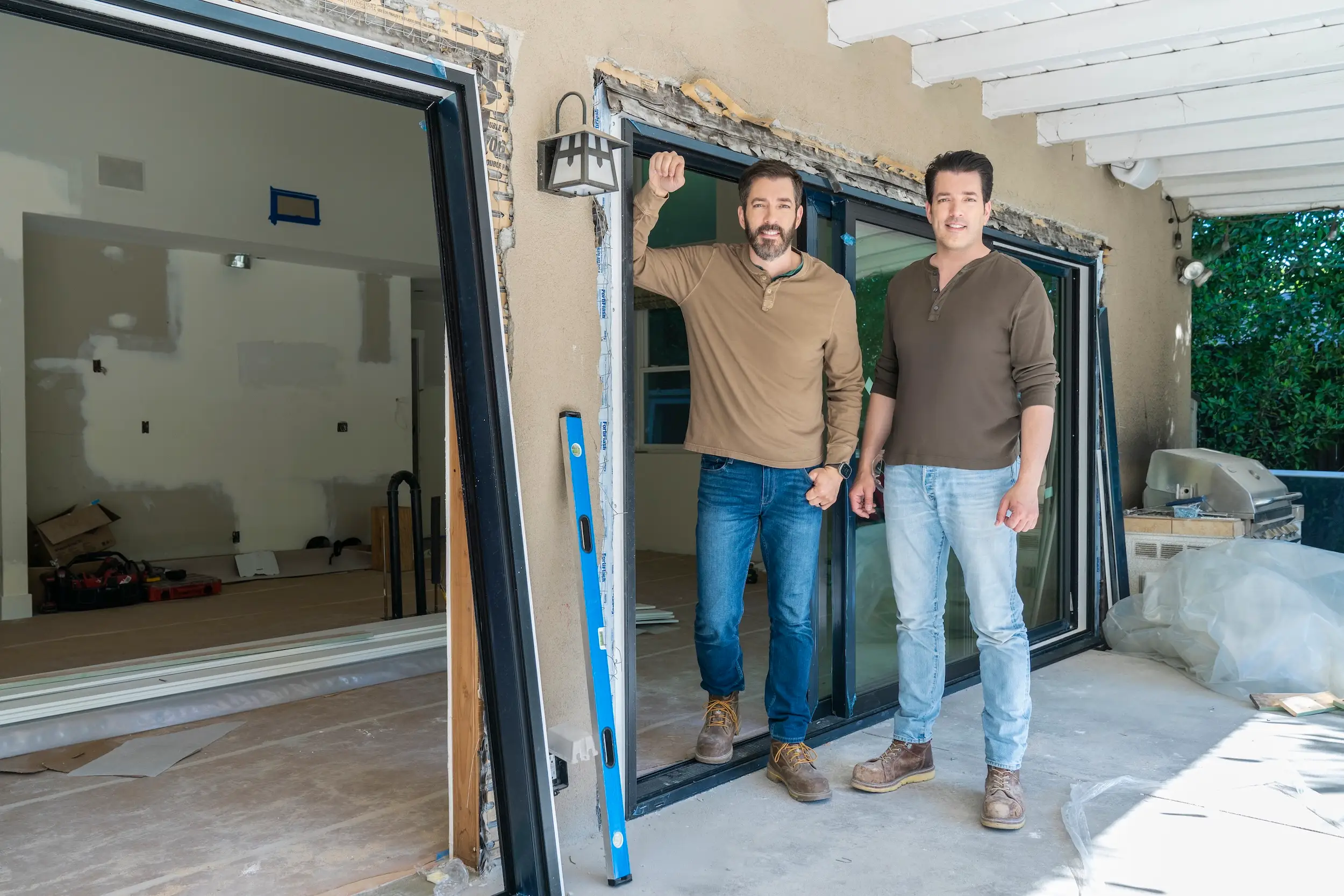 Twin brothers posing in front of a home during a renovation.