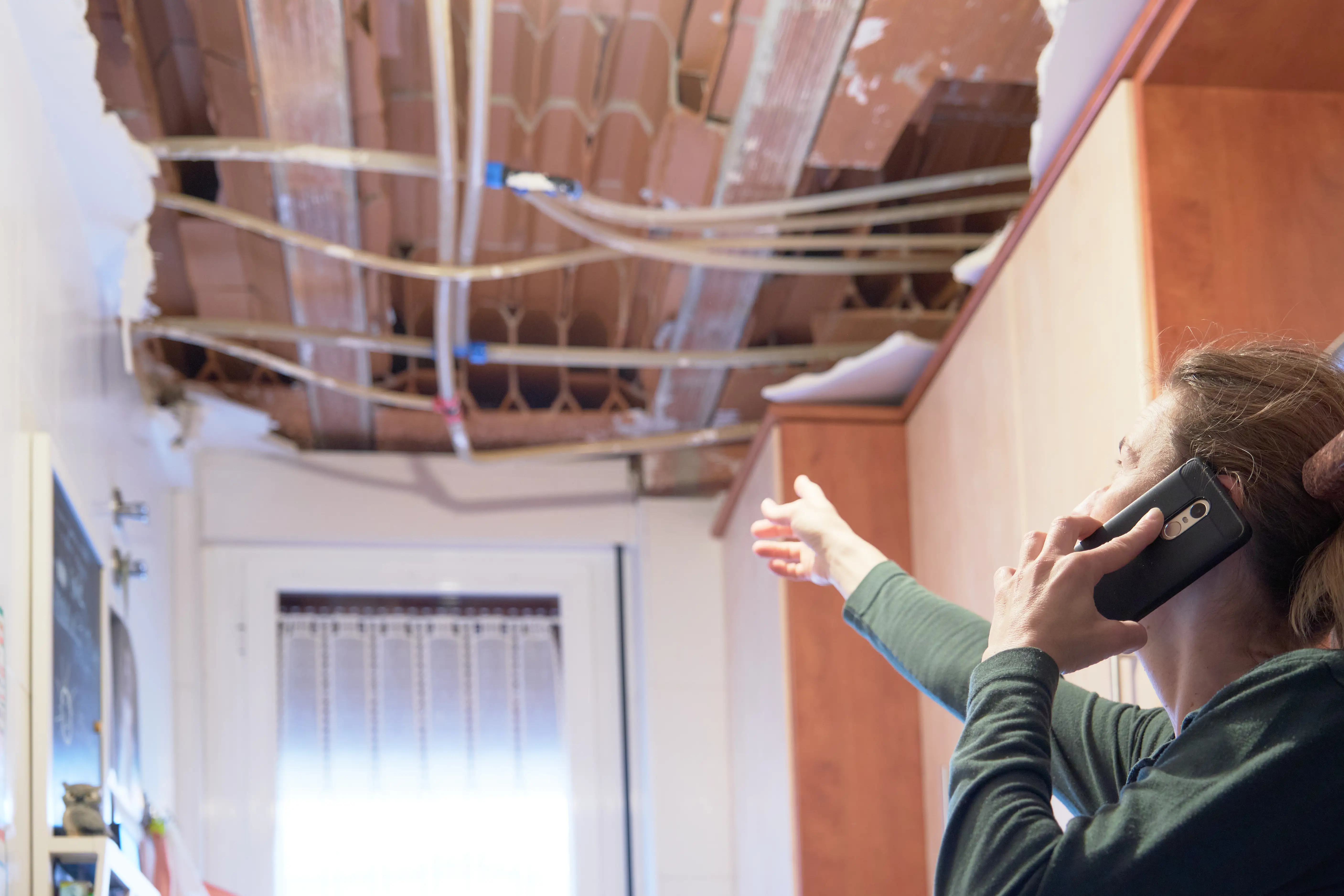 A woman on the phone pointing at her damaged ceiling.