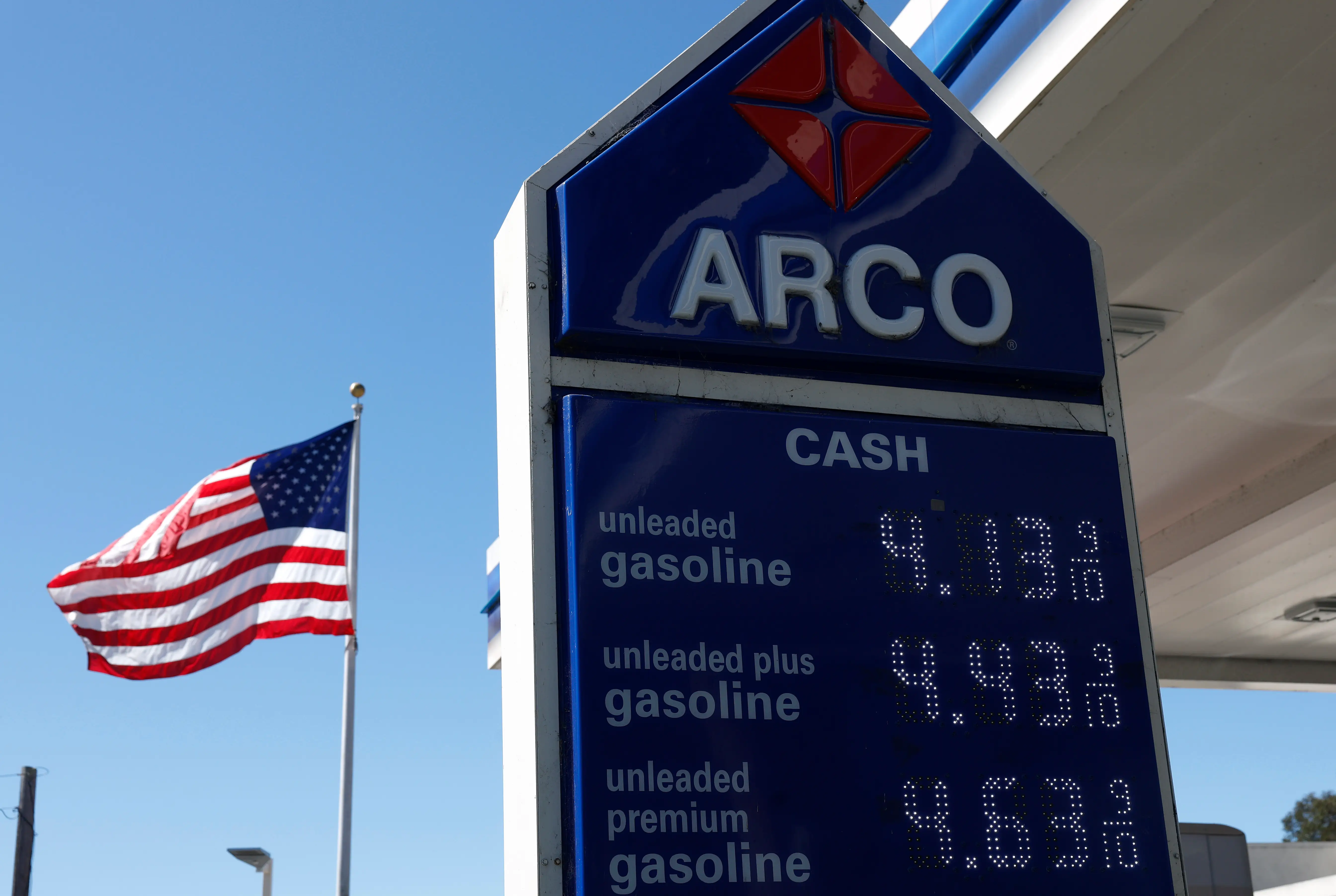 An Arco gas station sign shows the price for a gallon of regular gas at $4.13. An American flag blows in the wind in the background.