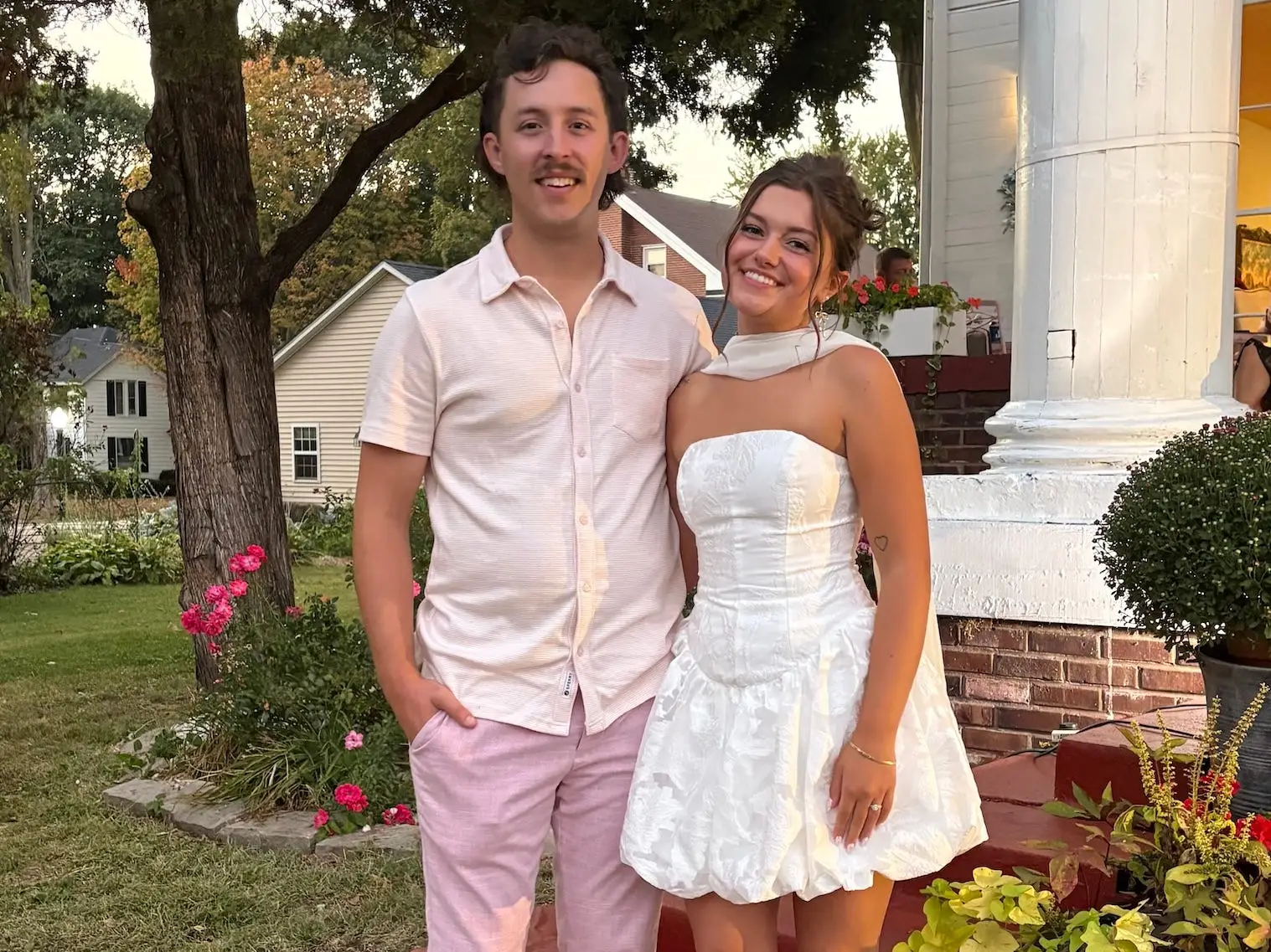 A man in pink and a woman in white stand in front a large building with white pillars.