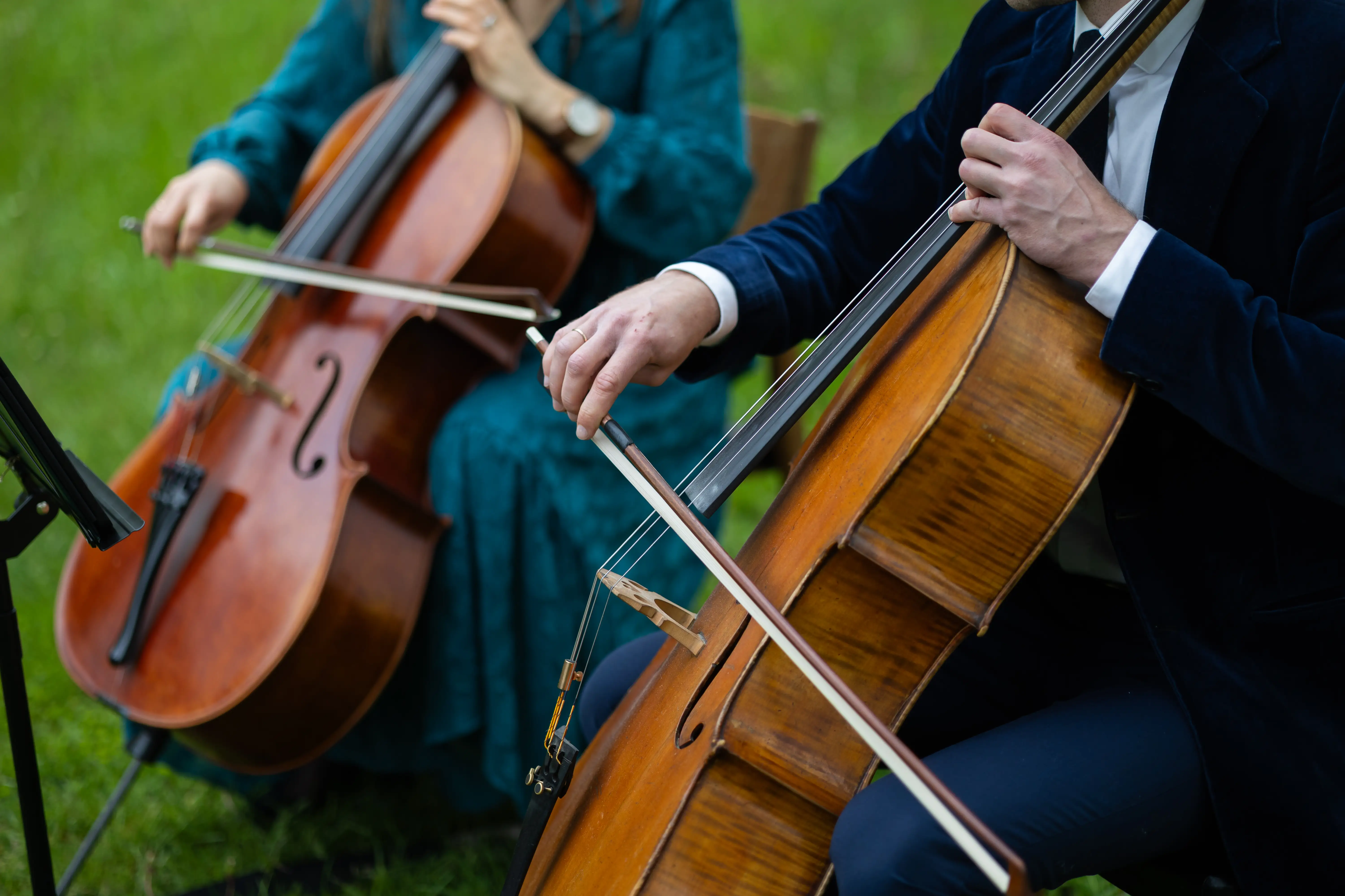 Two cello players playing outside in grassy field