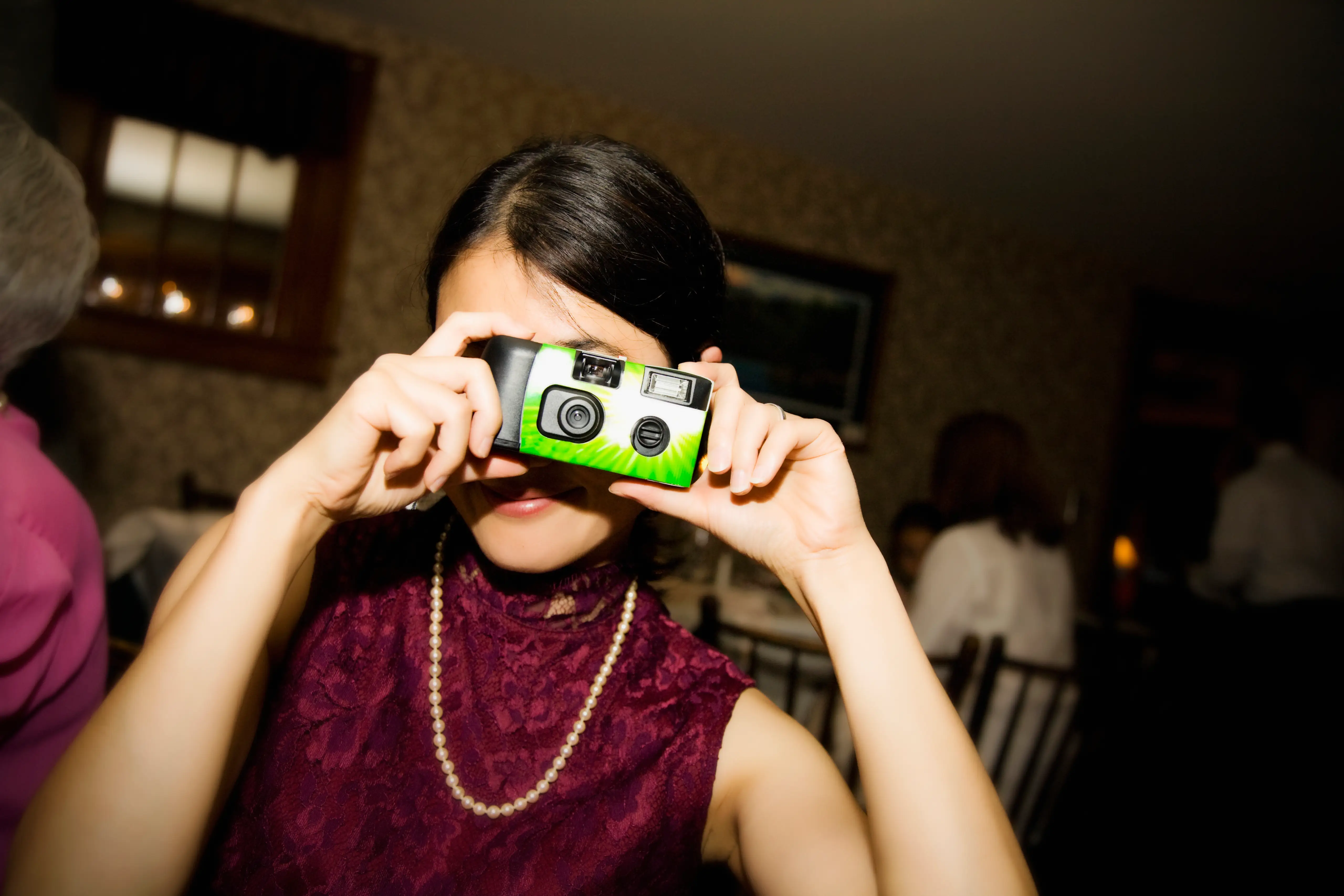 Woman with pearls on taking photo with disposable camera