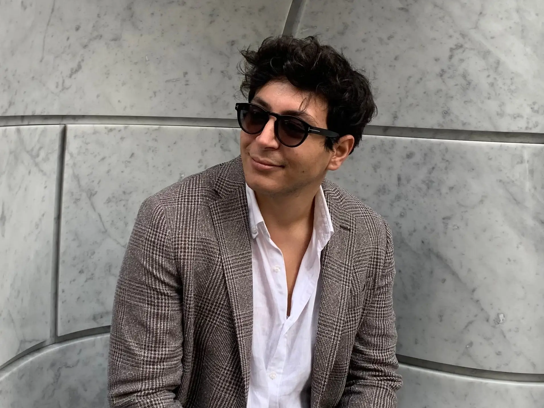 A man with wearing dark glasses and a plaid blazer.