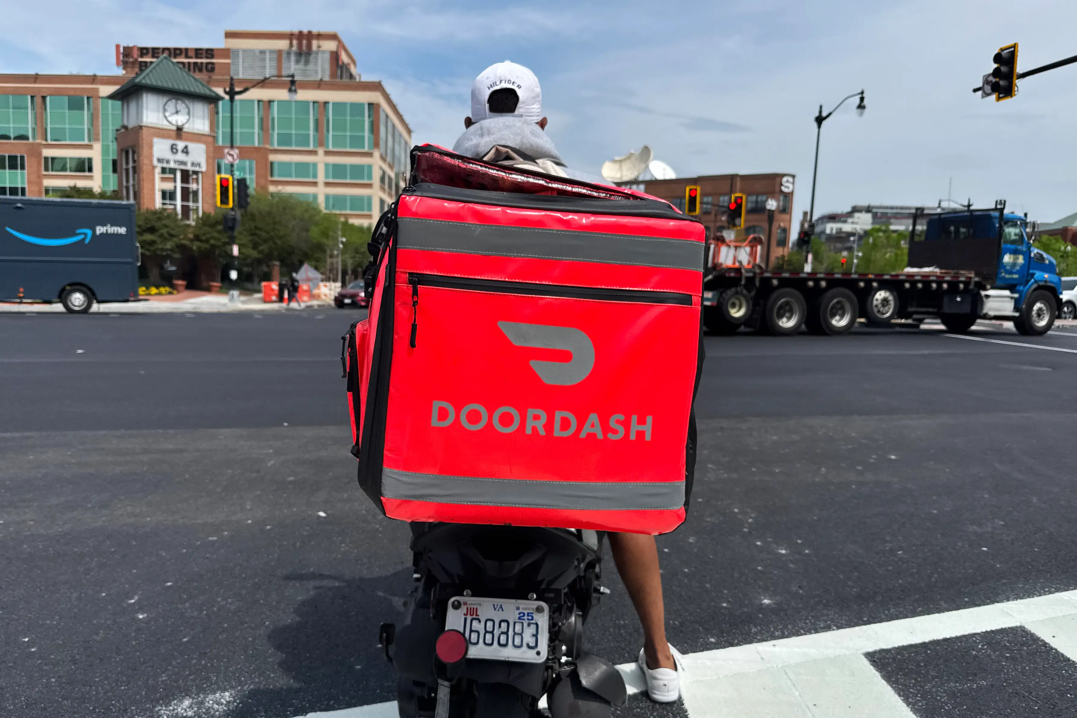 A moped rider with a red DoorDash insulated bag waits at an intersection in Washington, DC.