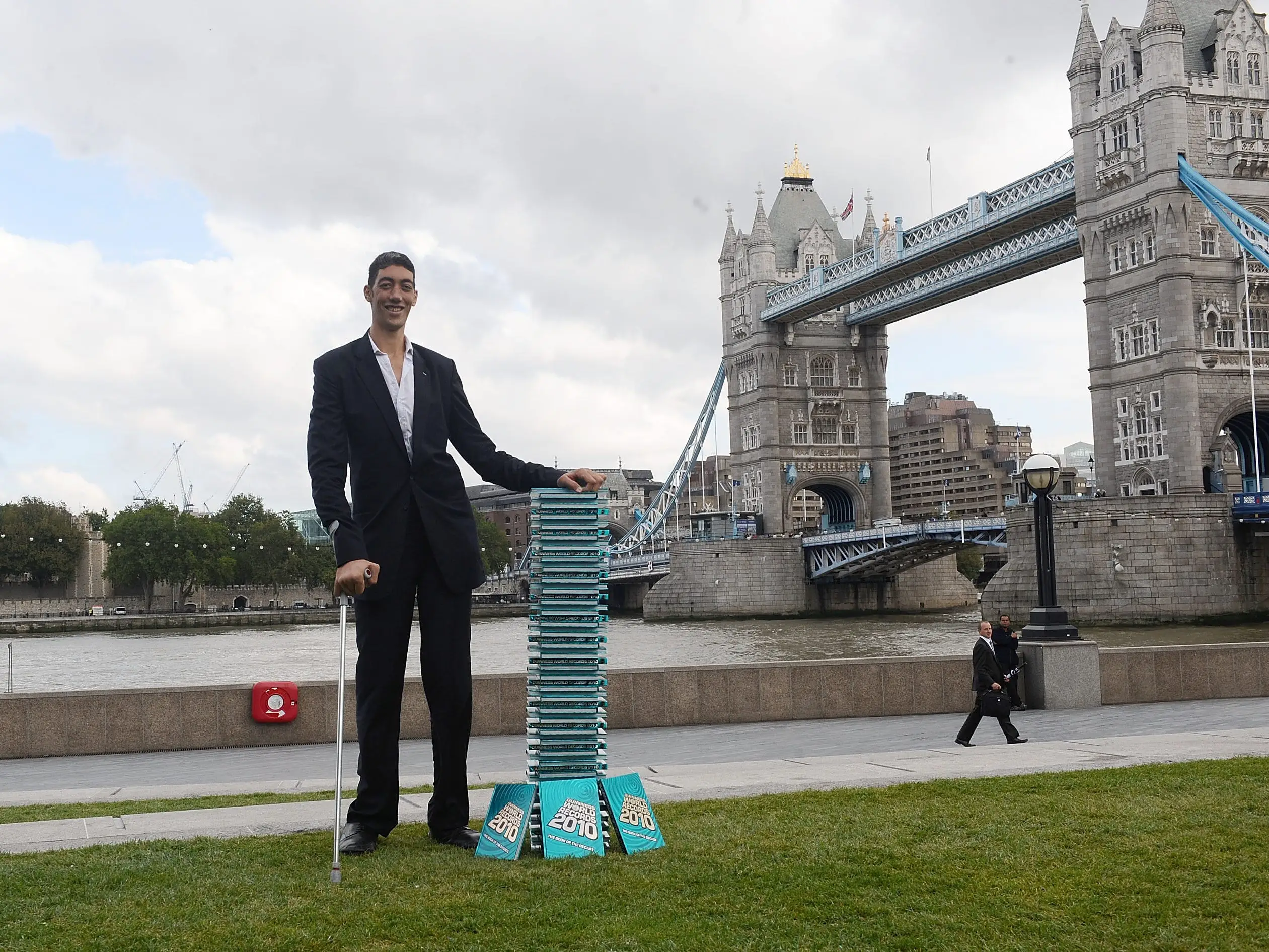 The world's tallest man, Sultan Kösen, poses in front of a stack of Guinness Book of World Records books.