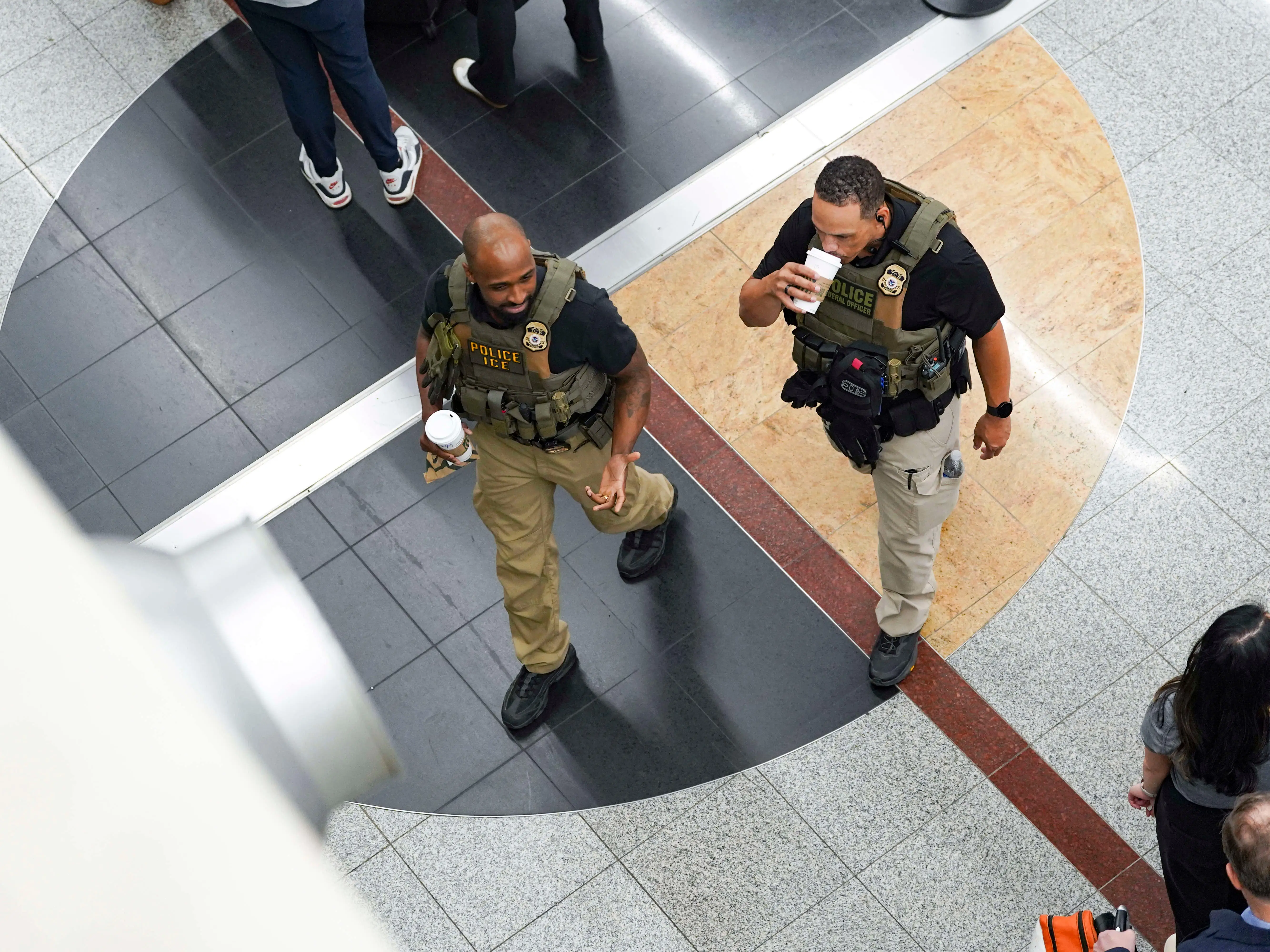 Ice agents walk through the airport drinking coffee as travelers stand in long lines at Atlanta Hartsfield-Jackson International Airport on March 23, 2026 in Atlanta, Georgia.